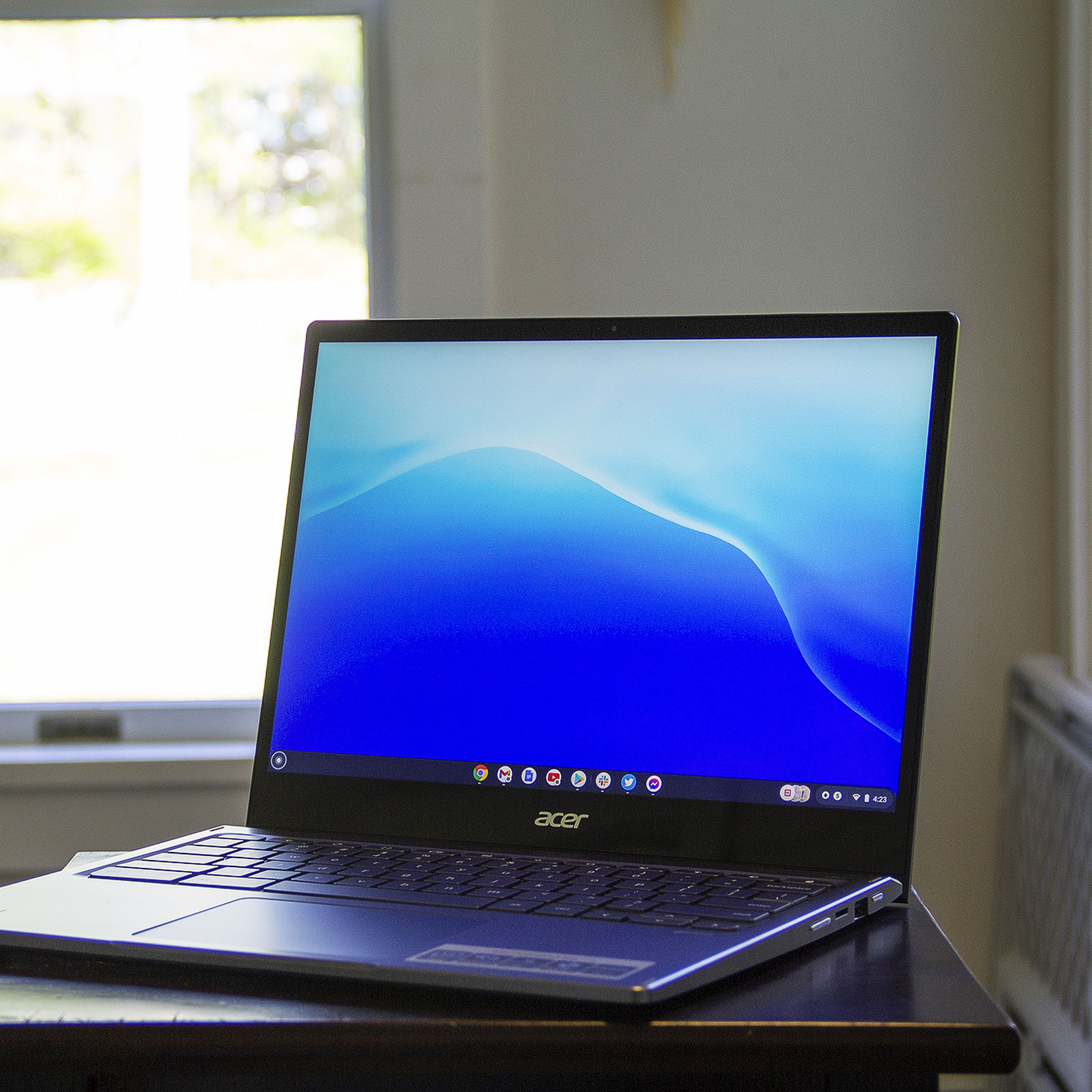 The Acer Chromebook Spin 713 on a small table in front of a bright window. The screen displays a blue pattern.
