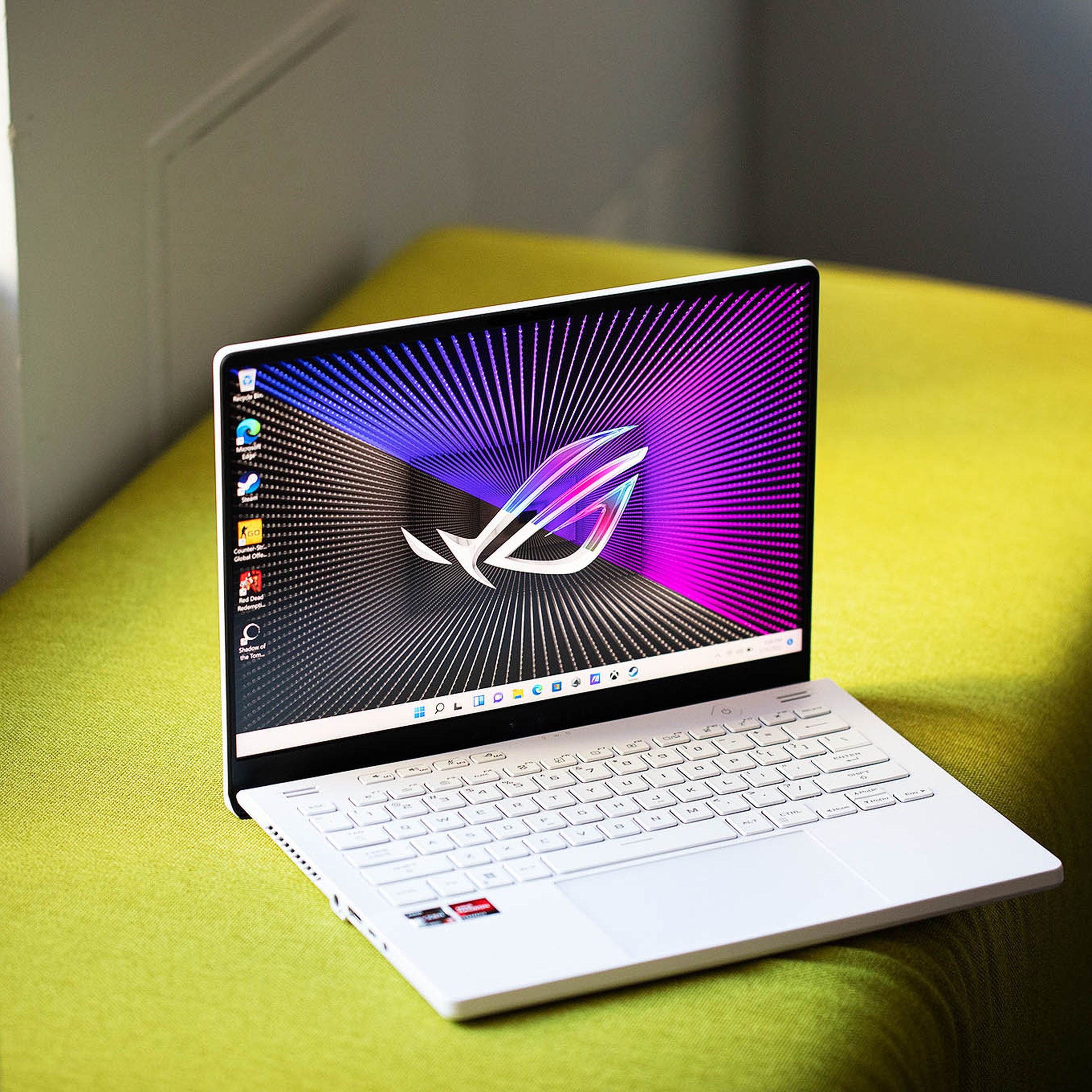 The Asus ROG Zephyrus G14 on a green bench open angled slightly to the right. The screen displays a black and purple background with the ROG logo.