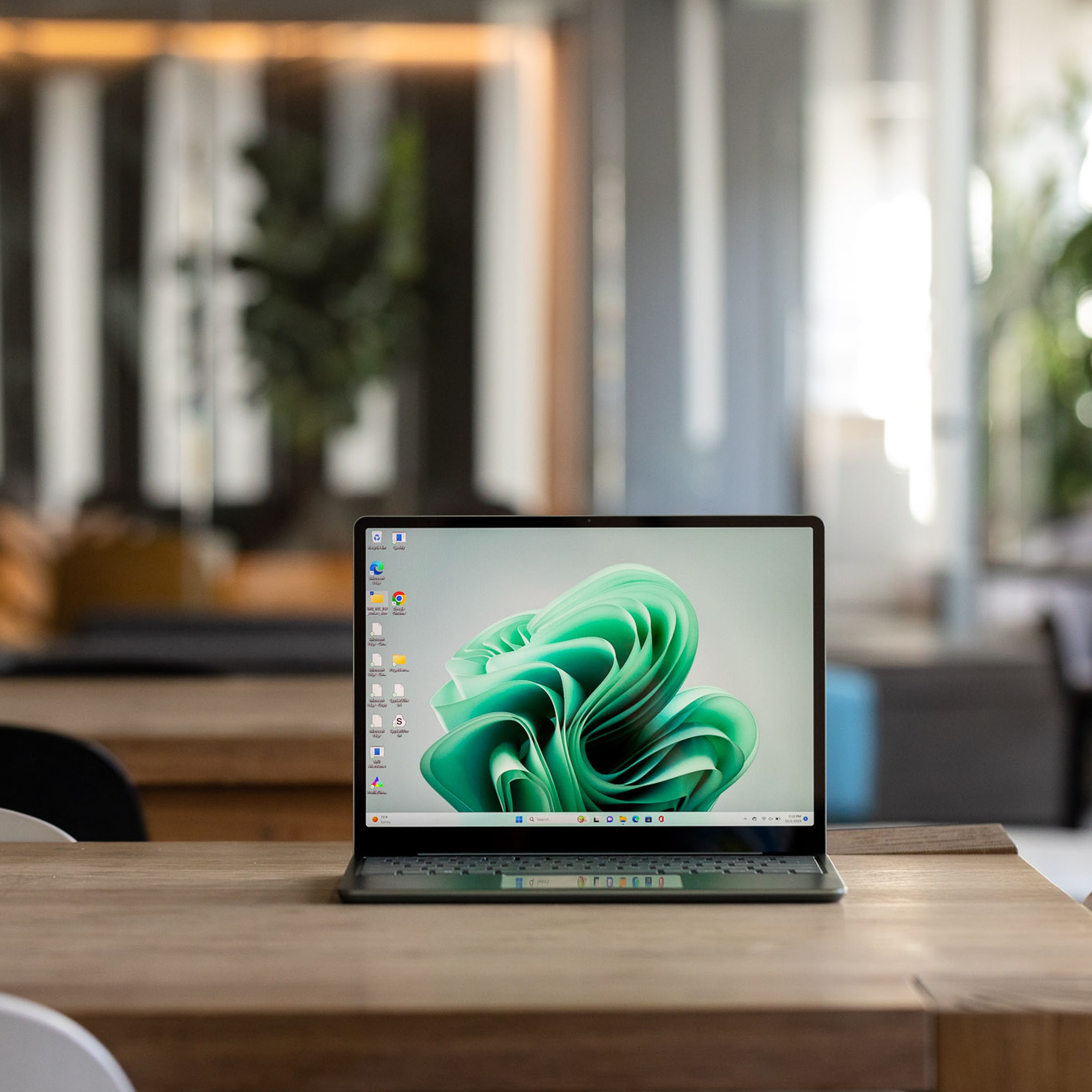 The Microsoft Surface Laptop Go 3 displaying a green Windows desktop on a table in a cafe setting.