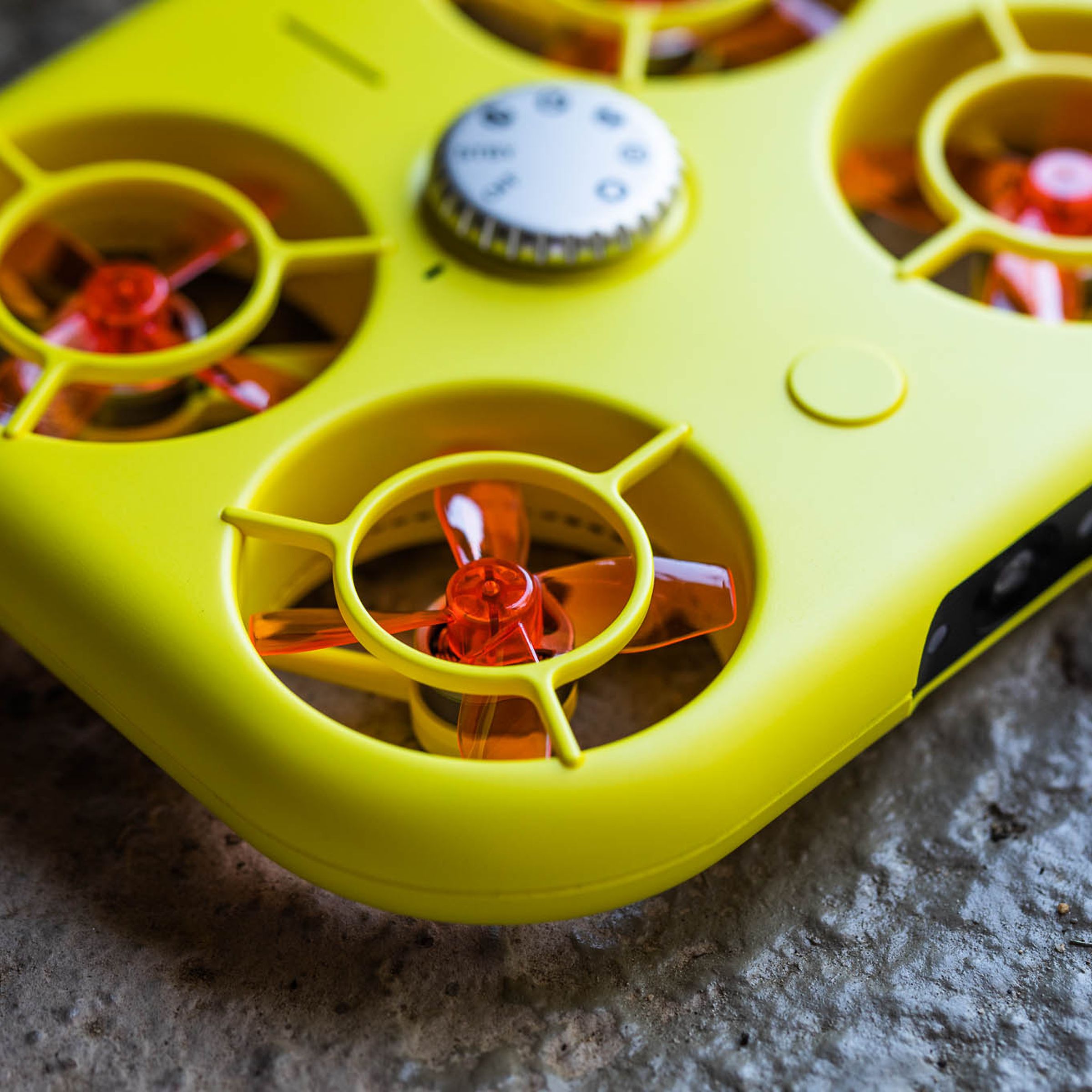 A yellow drone shaped like a rounded rectangle instead of exposed blades — it has translucent orange propellers within its boxy but thin frame.