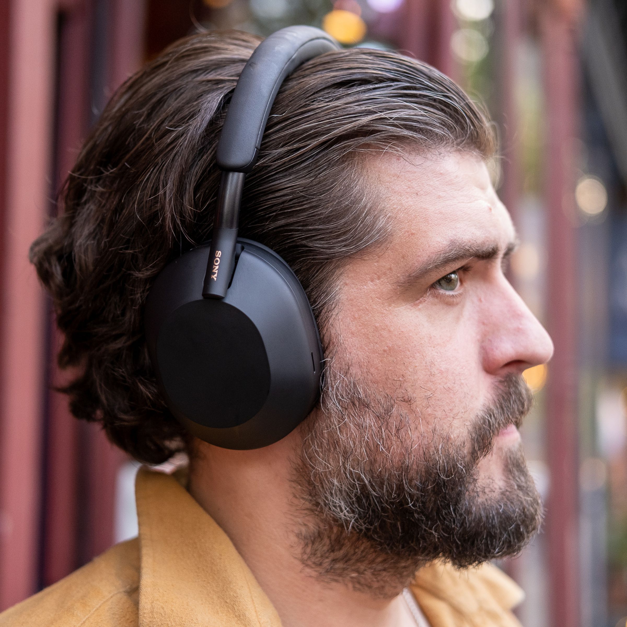 A man wearing Sony’s black WH-1000XM5 noise-canceling headphones outside.
