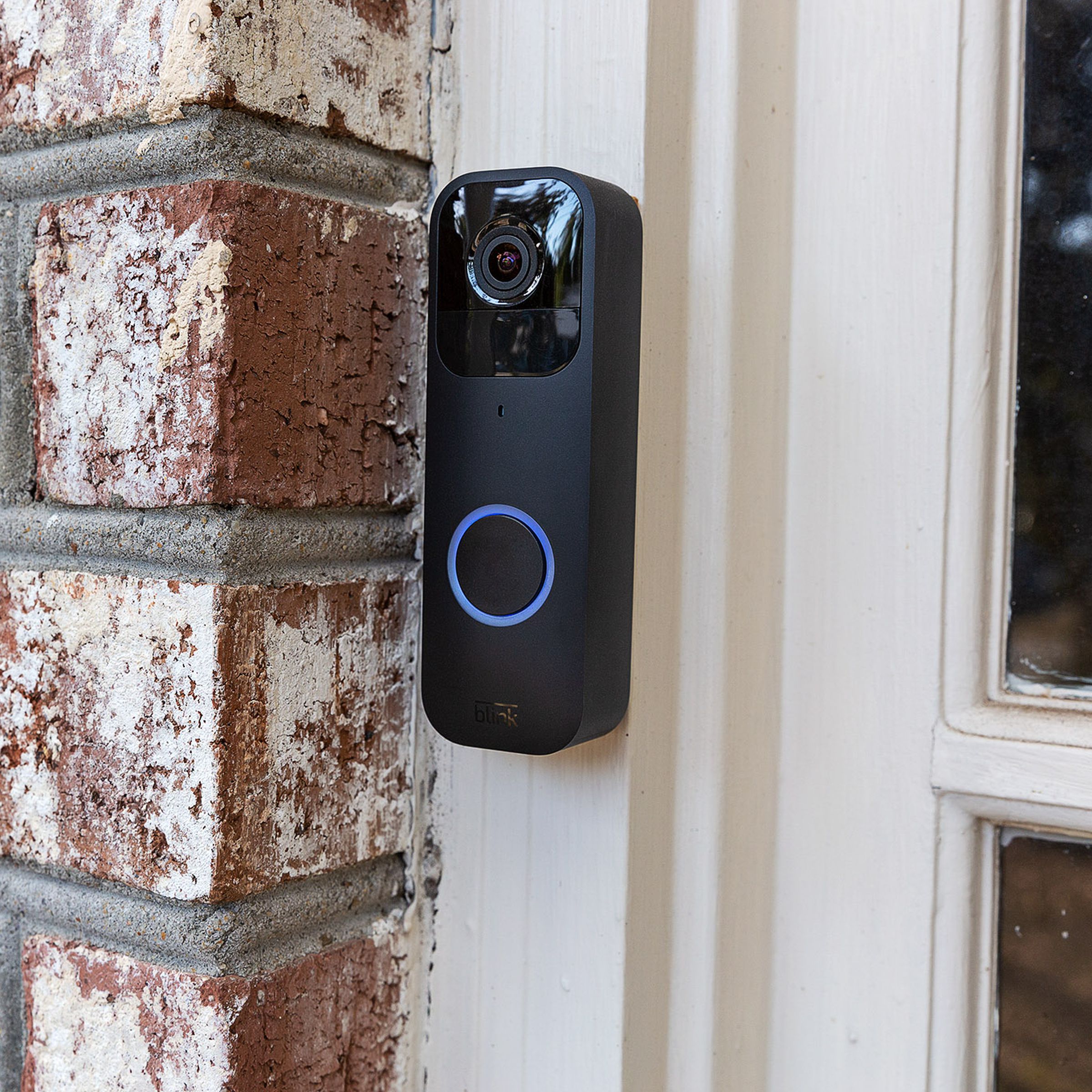 The black Blink Video Doorbell hung up on a brick wall outside of a house.
