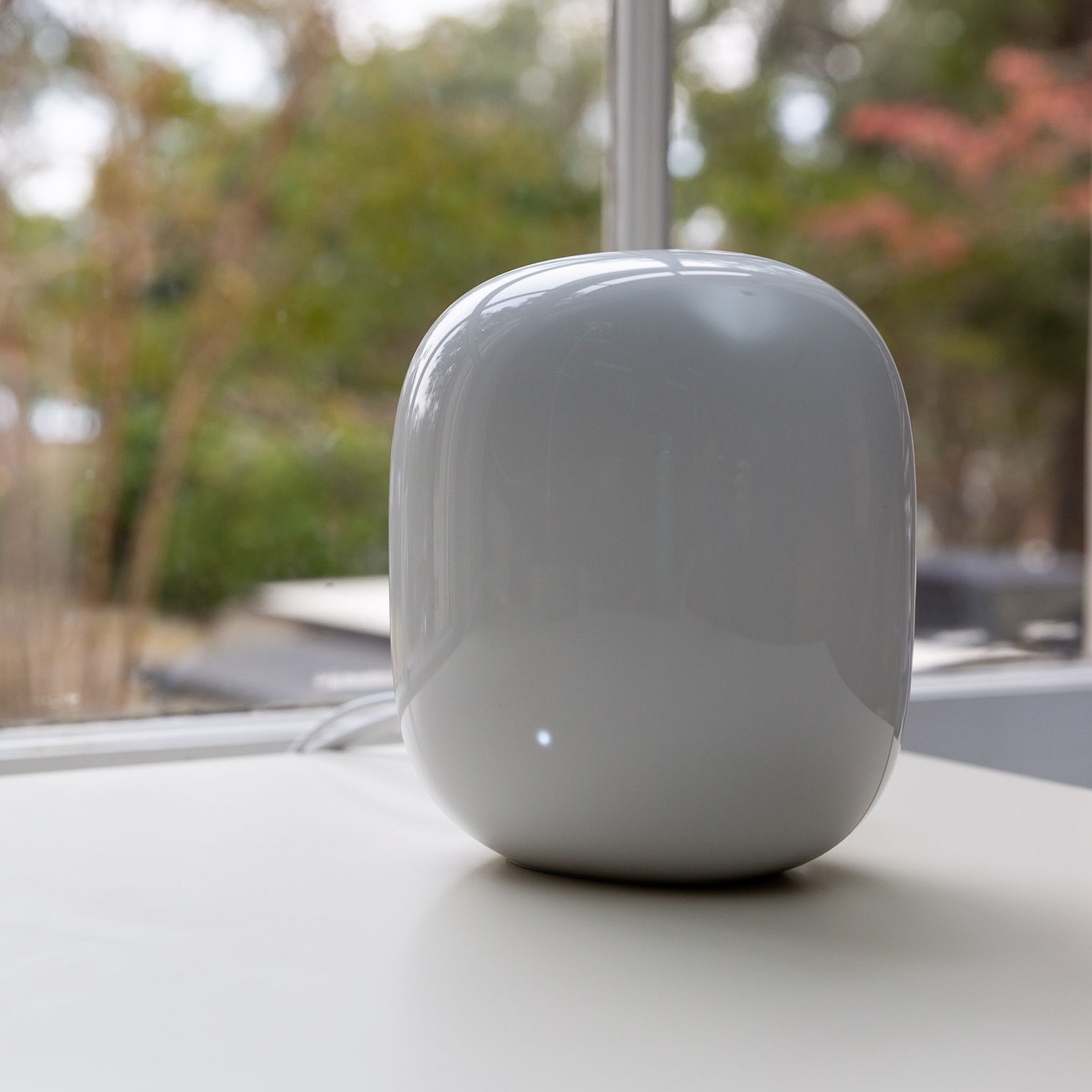 White Google Nest Wifi Pro router on a white table, in front of a window.