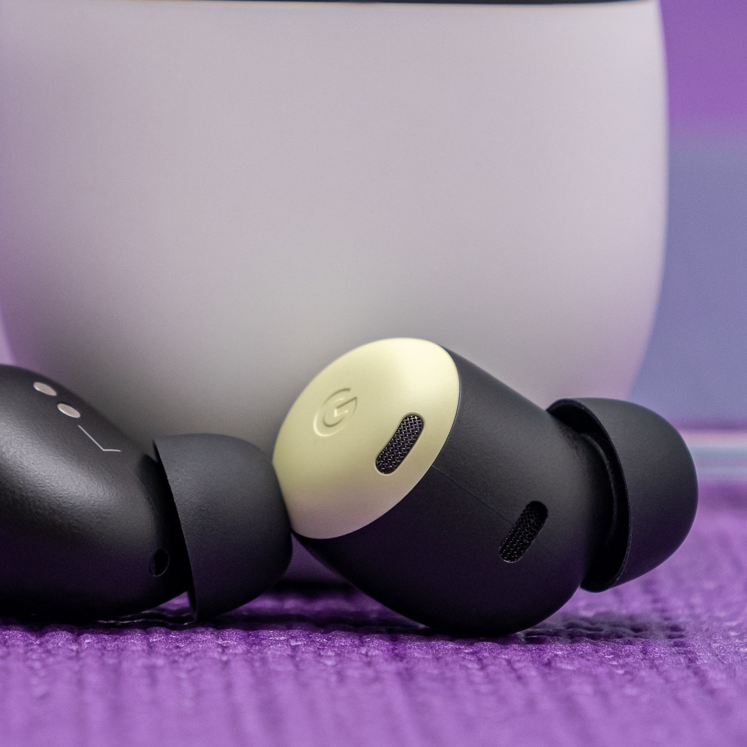 Google's Pixel Buds Pro earbuds, in lemongrass yellow, rest at the foot of their white charging case on a tabletop.