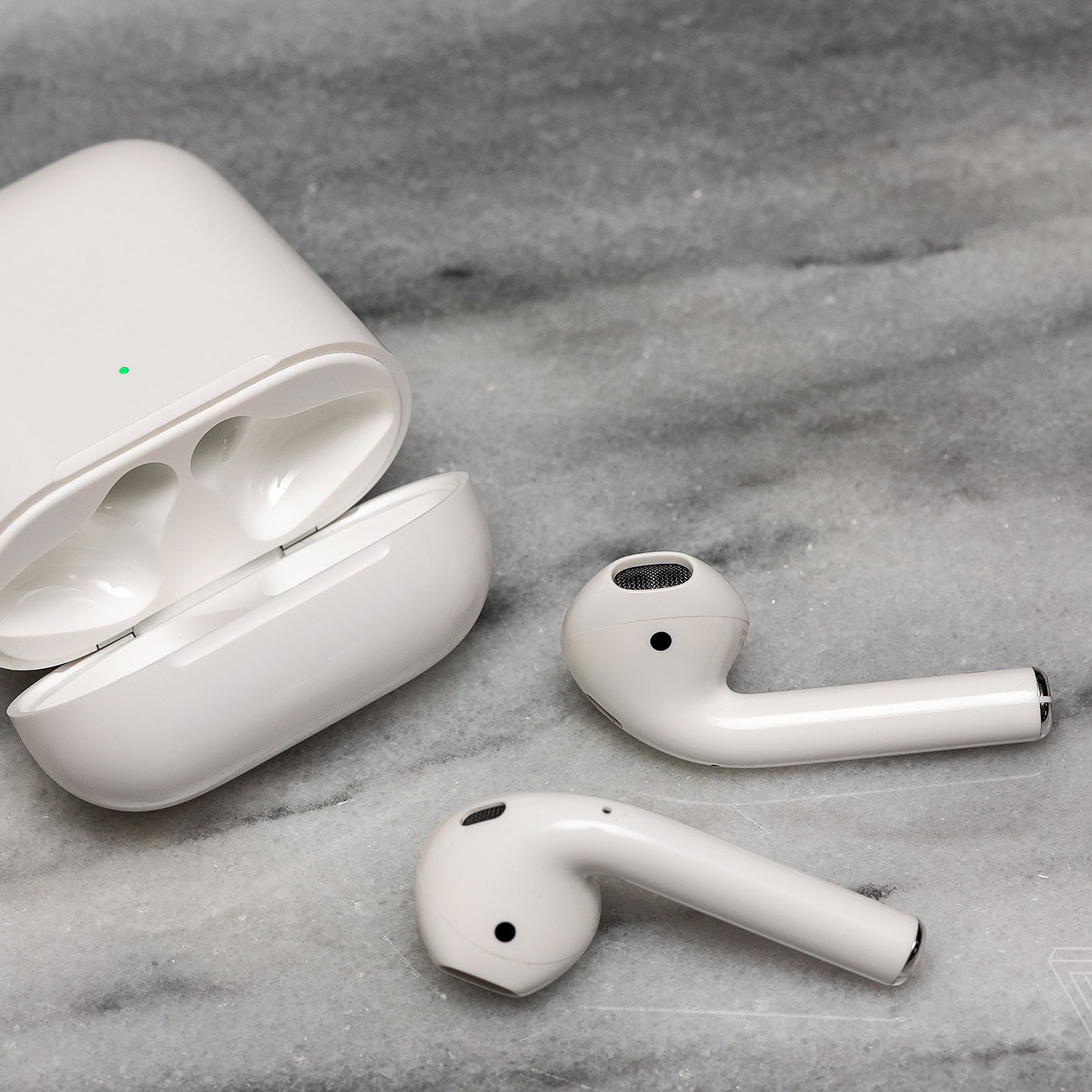 The second-generation AirPods near their charging case on a white surface.