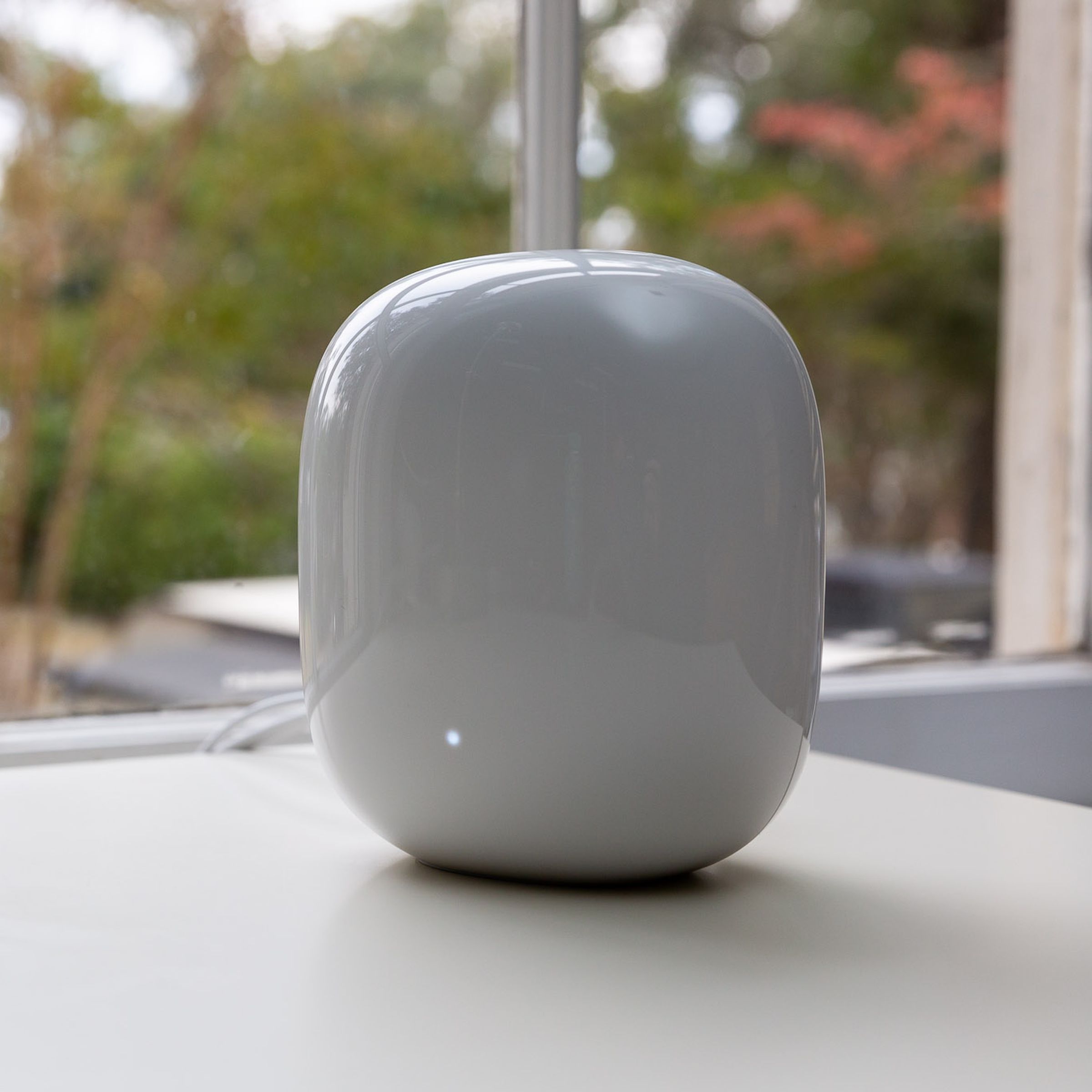 Bir pencerenin önünde beyaz bir masada beyaz Google Nest Wifi Pro yönlendirici.