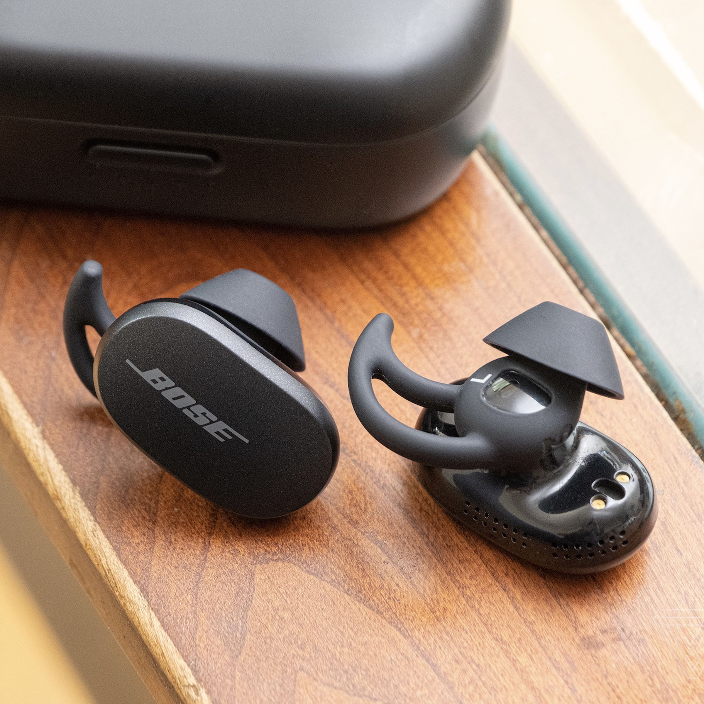The Bose QuietComfort Earbuds on a table beside the carrying case.