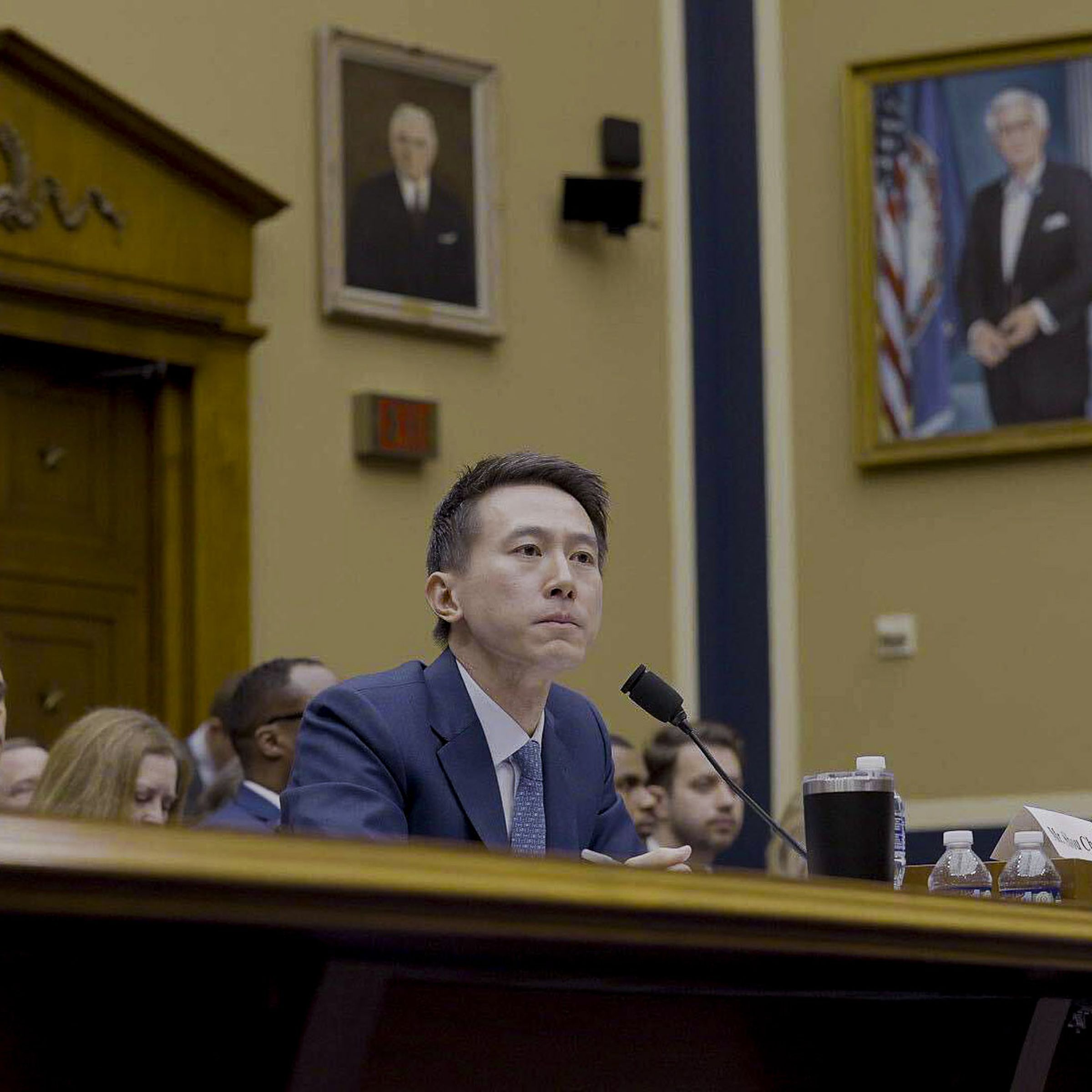 Shou Zi Chew is seated for a hearing. Portraits of American political figures hang on the wall behind him.