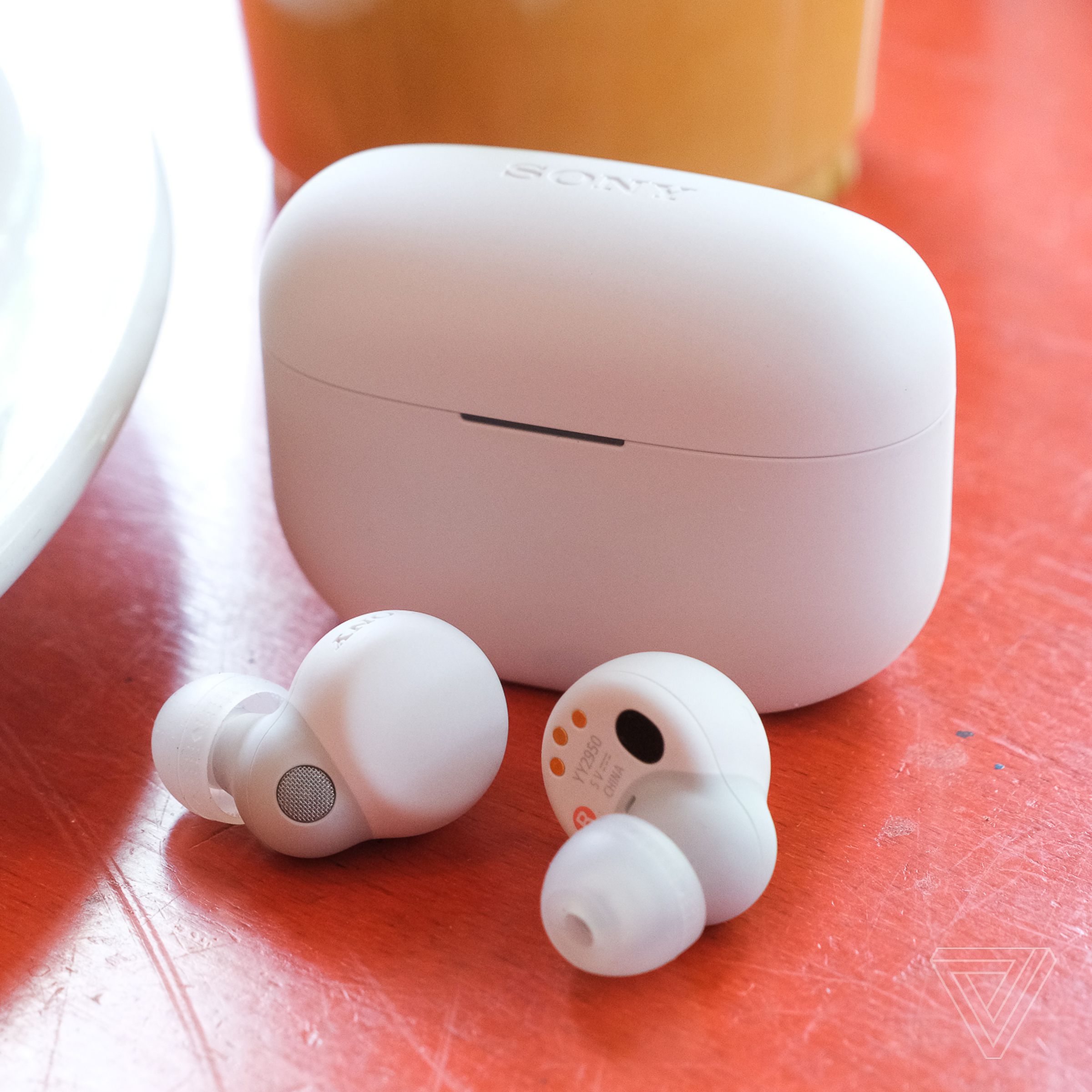 The white Sony LinkBuds S earbuds resting on a table outside their case, beside a plate of food.