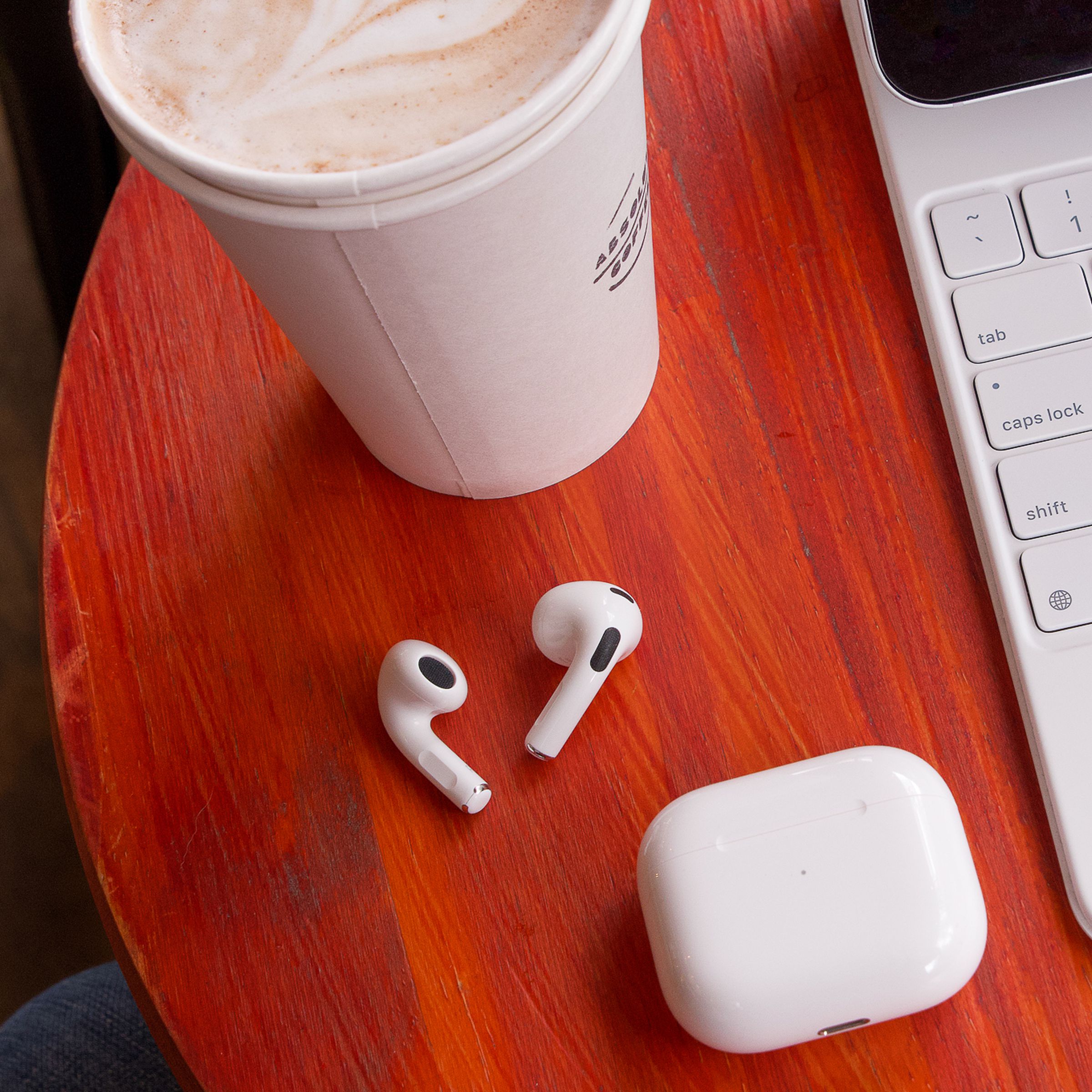 An image of Apple’s AirPods on a table beside a cup of coffee.