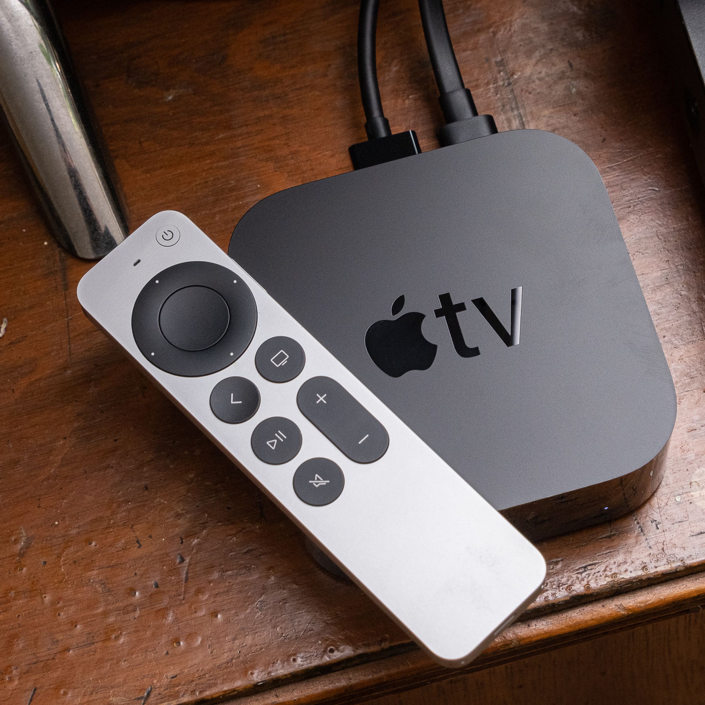 A 2021 Apple TV and its Siri remote sit atop a wooden entertainment center.