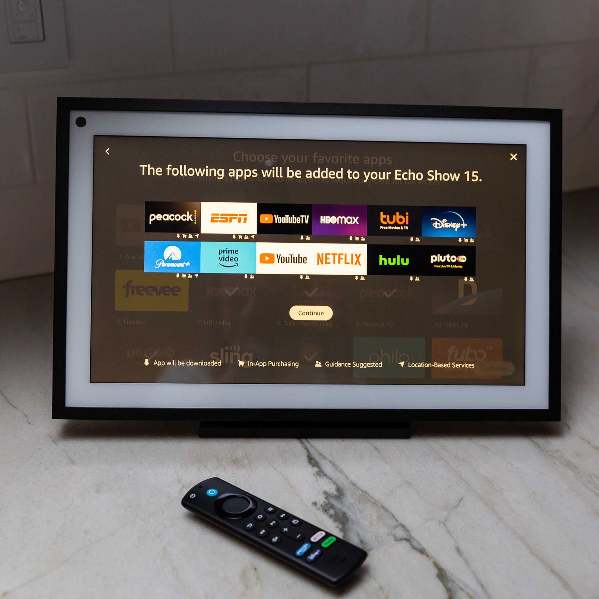 A Show 15 smart display on a kitchen counter with an Alexa remote control.