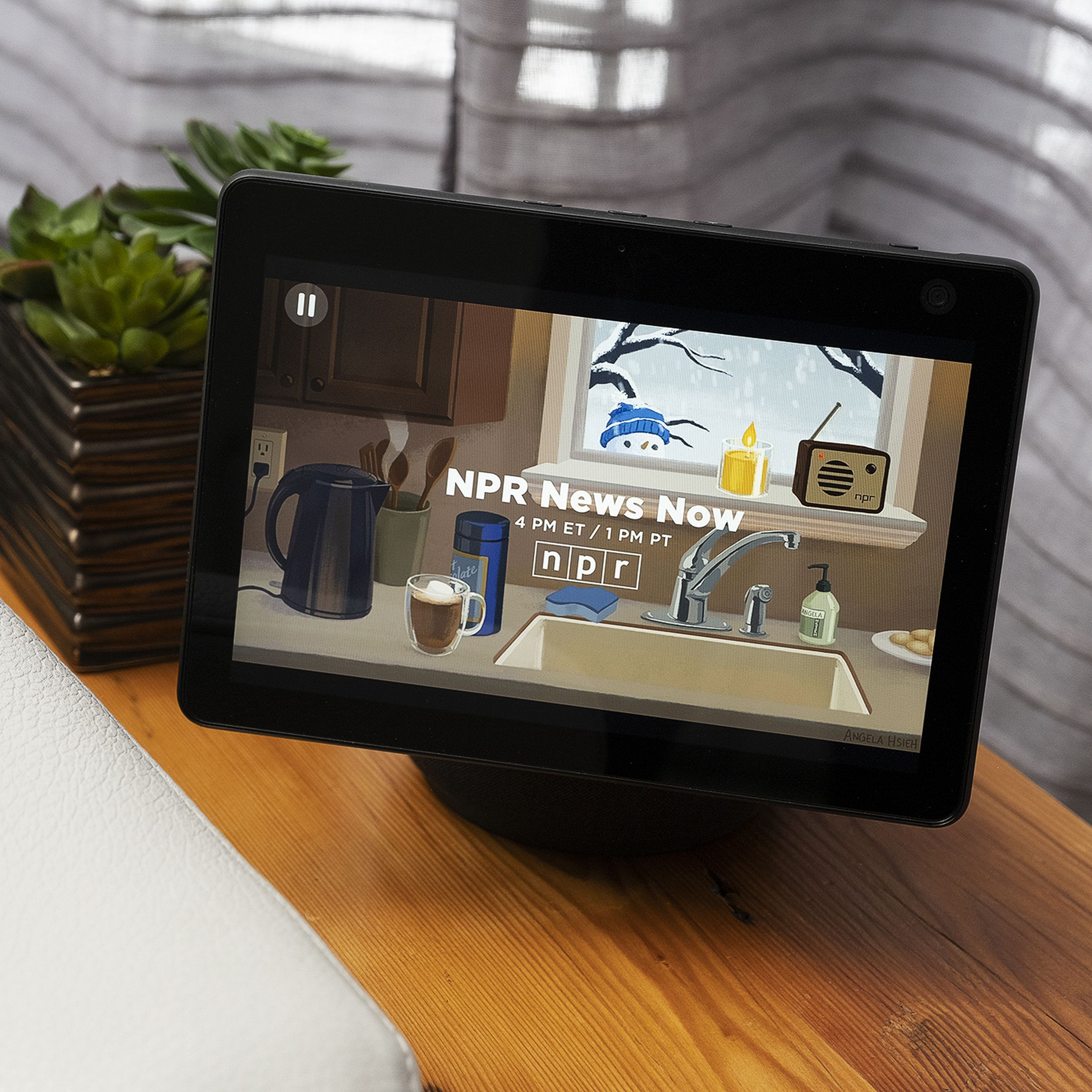 An Echo Show 10 device sitting on a piece of wood furniture beside a couch.