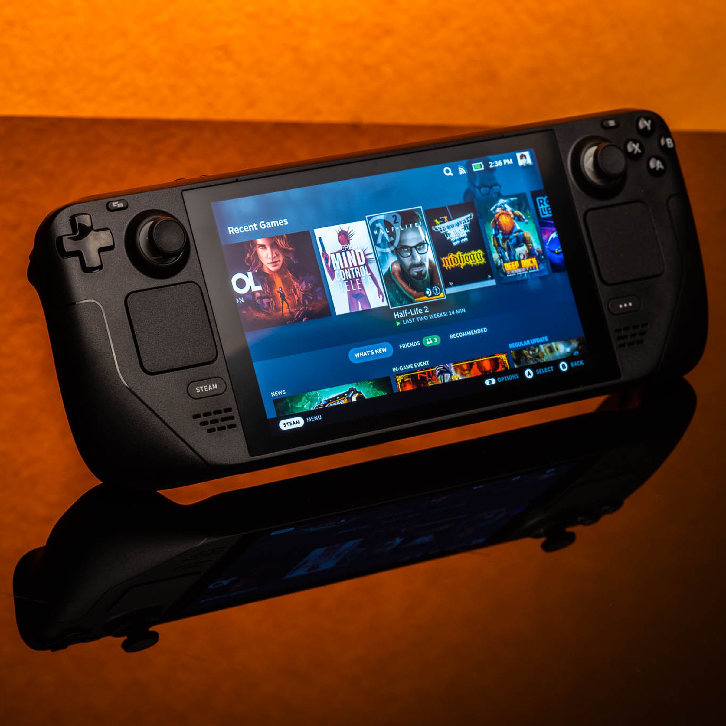 The Valve Steam Deck gaming handheld sits on a reflective table, with an orange background.