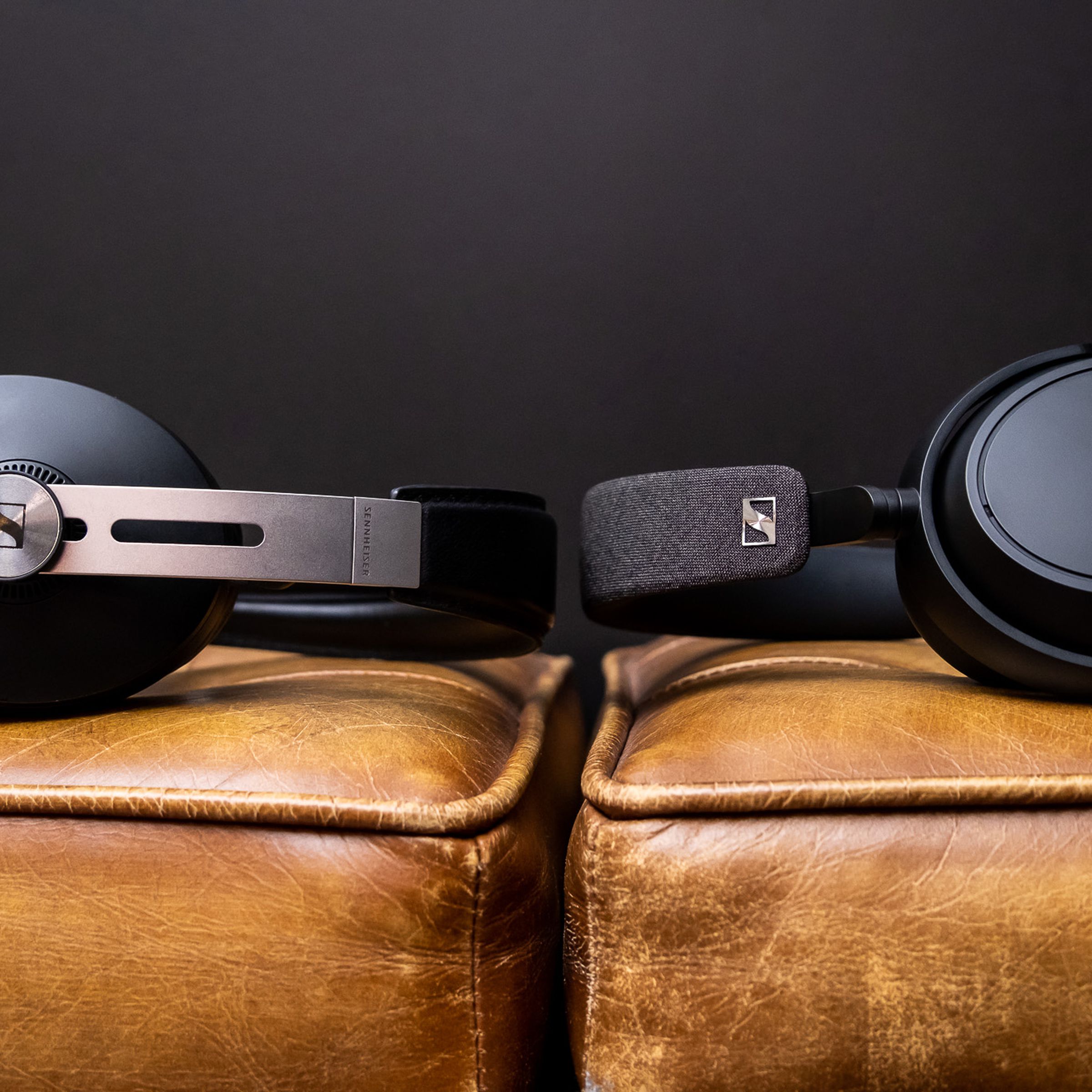 The Sennheiser Momentum 3 and Sennheiser Momentum 4 headphones facing each other while lying on a couch.