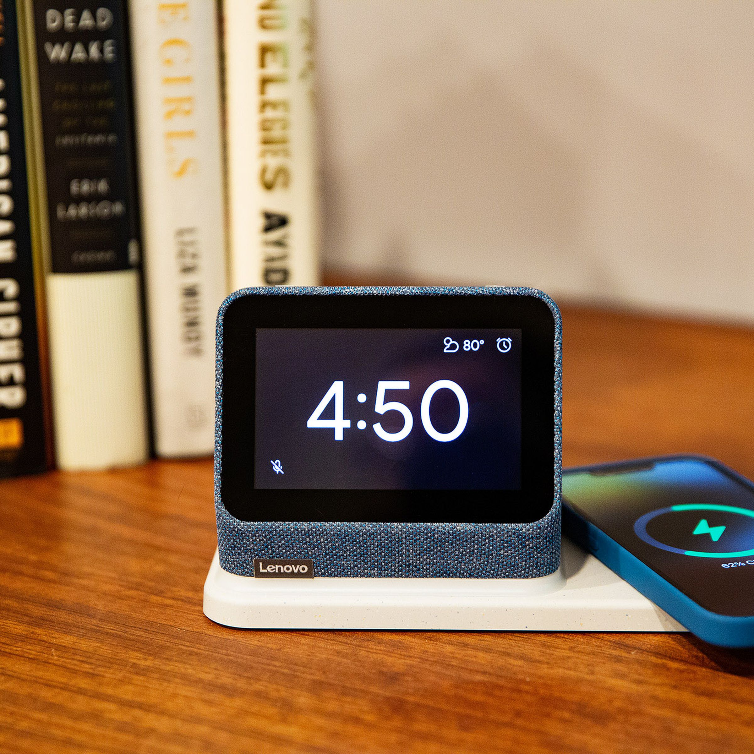 The Lenovo Smart Clock 2 displaying the time while a phone wirelessly charges on its dock.