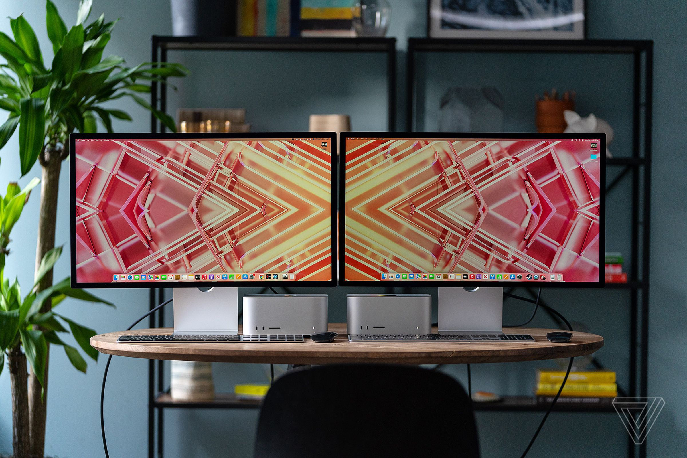 Two Mac Studio models and two monitors side by side on a wooden table in a living room space.