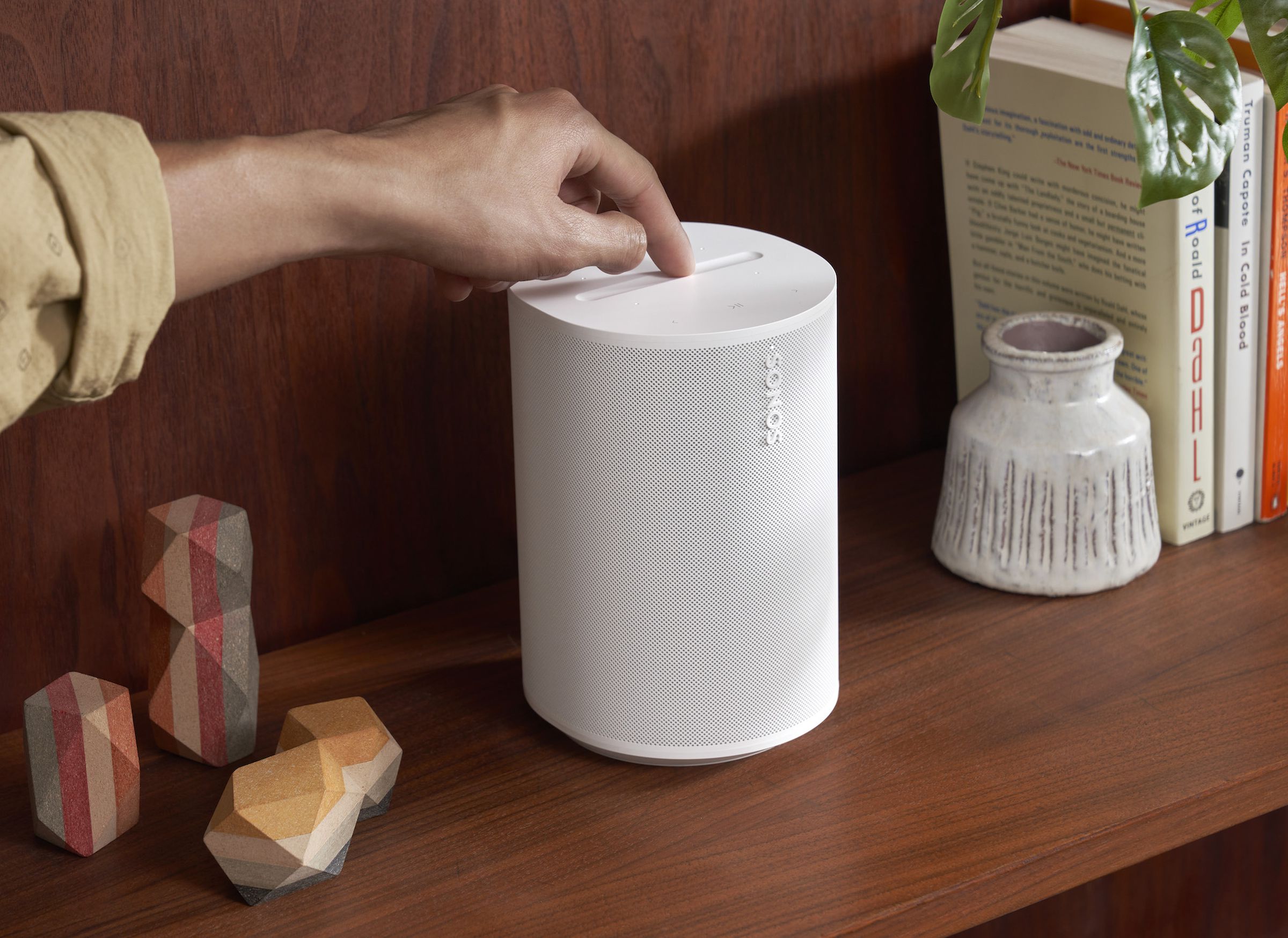 A marketing image of the Sonos Era 100 speaker on a wood shelf.