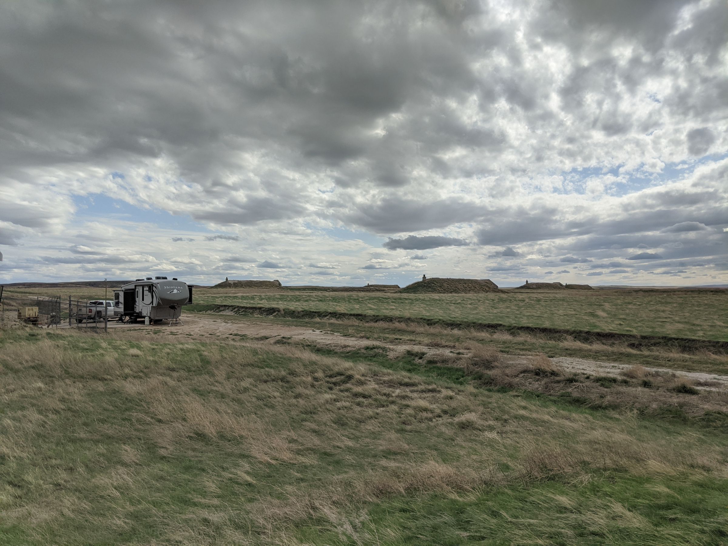 A landscape photo showing Tom and Mary’s truck, camper van and neighboring bunkers with a cloudy sky.