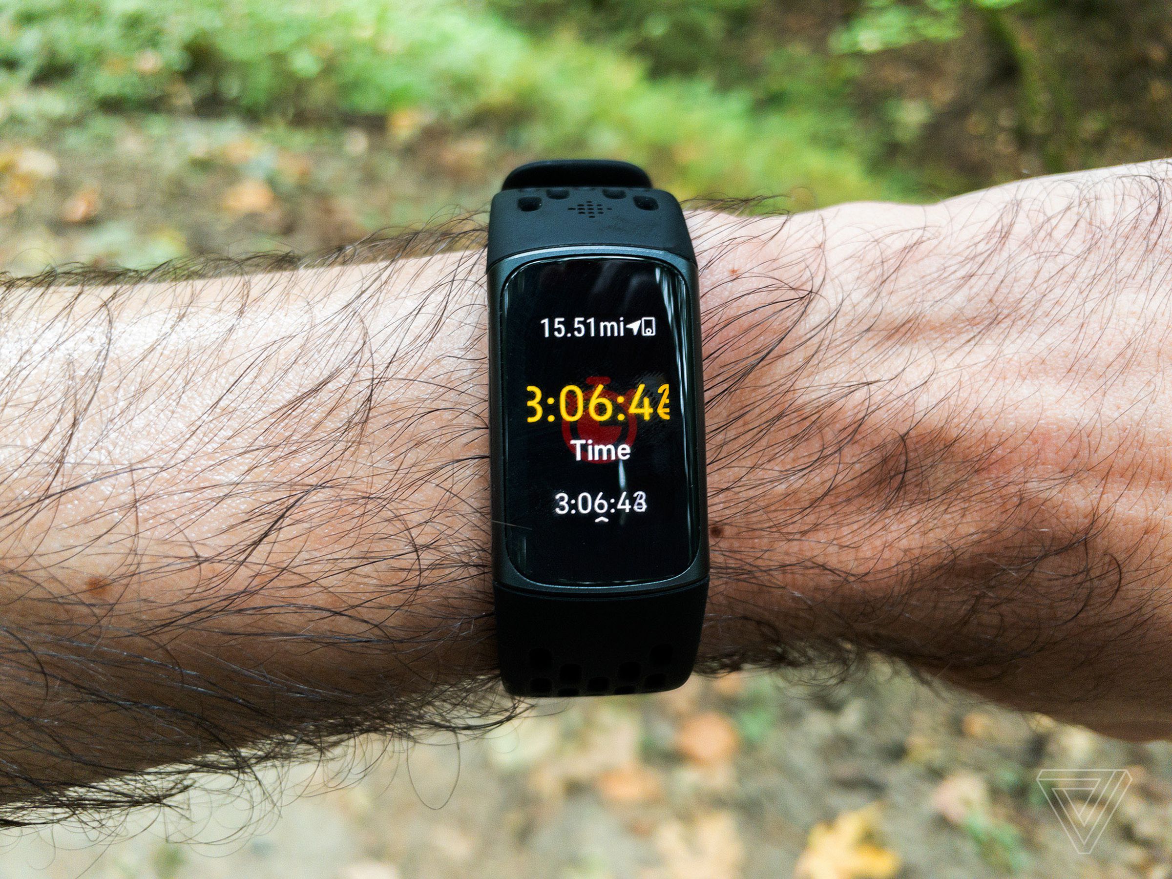 Close-up of a Fitbit Charge 5 worn on a person’s left wrist. There appears to be a forest path in the background. The person seems to be on a long run; the display reads “15.51 mi” with an elapsed time of 3 hours, 6 minutes, and 41 seconds. 