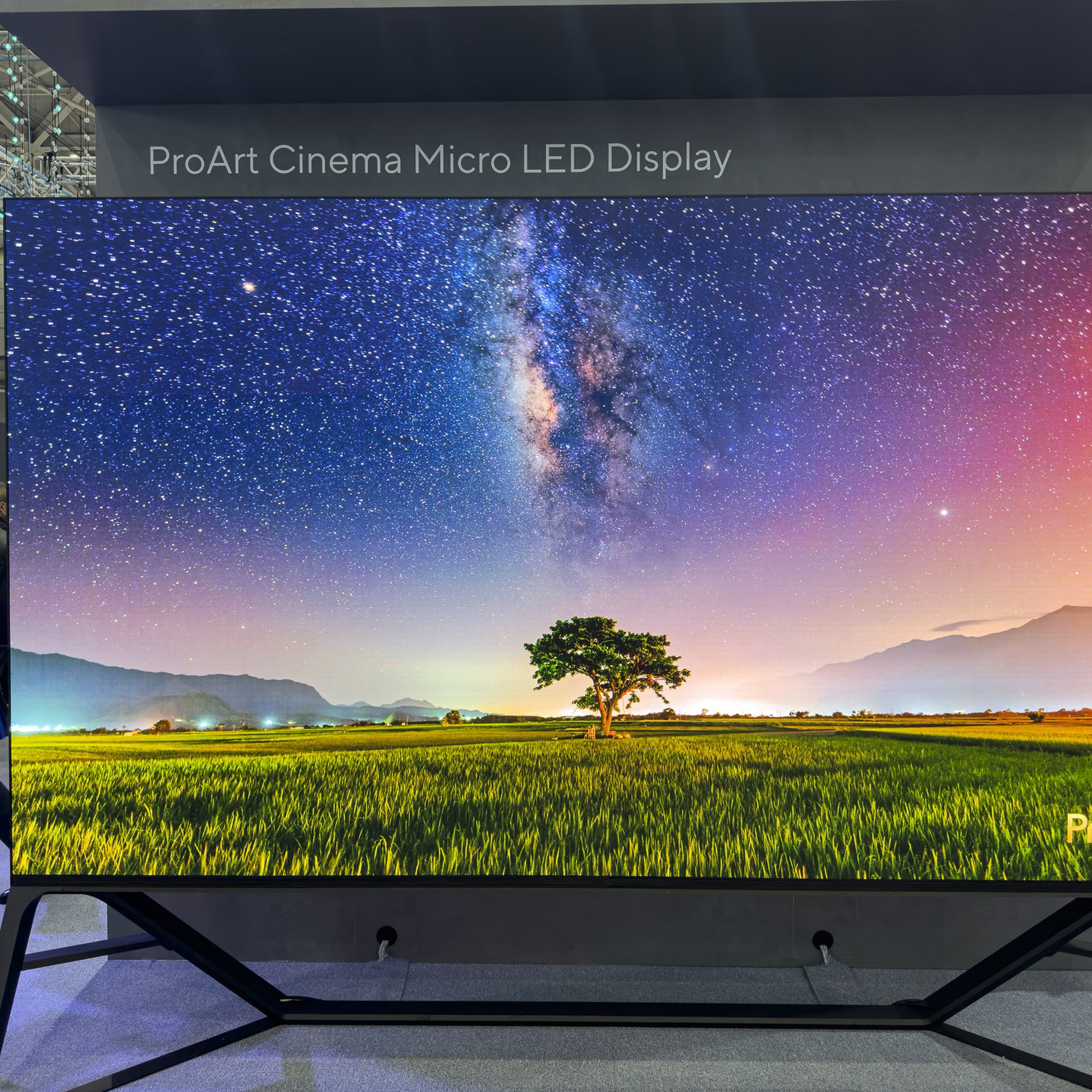 The Asus ProArt Cinema PQ07 displaying an outdoor scene with a tree and a colorful sky on the Computex 2023 show floor.