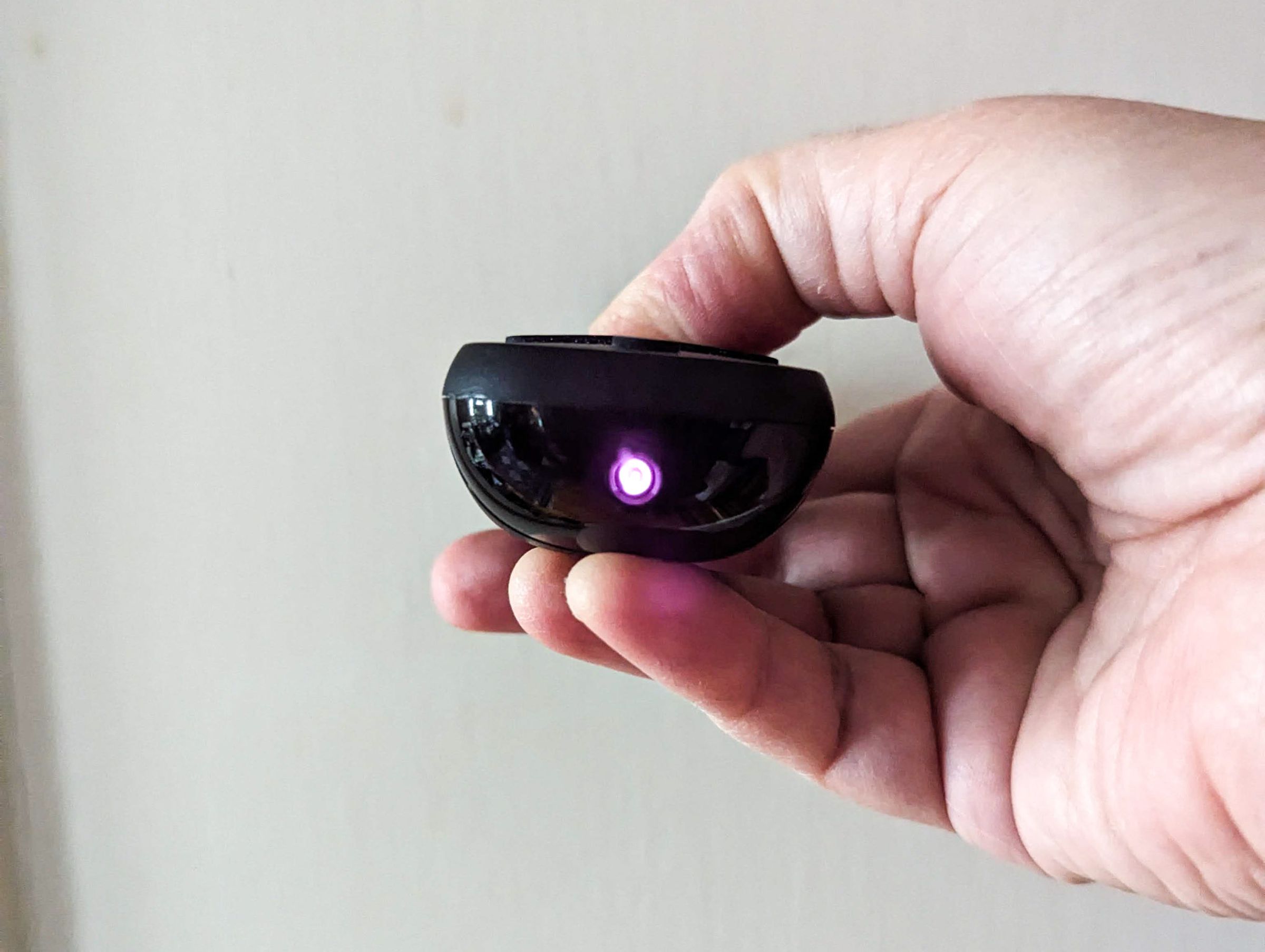 Photo of hand holding a TV remote with a small, visible pinkish light at the tip.