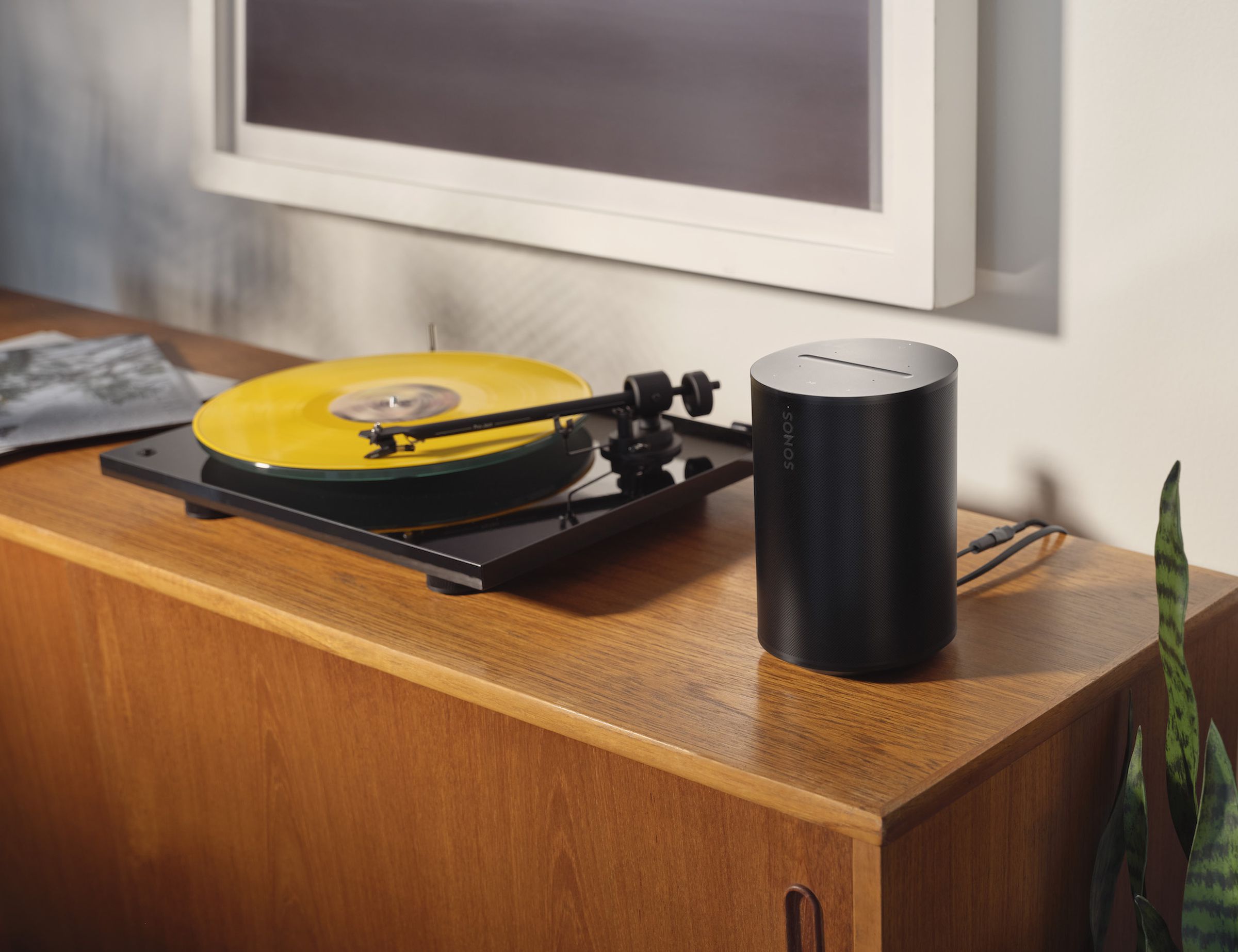 A photo of a Sonos Era 100 beside a turntable.