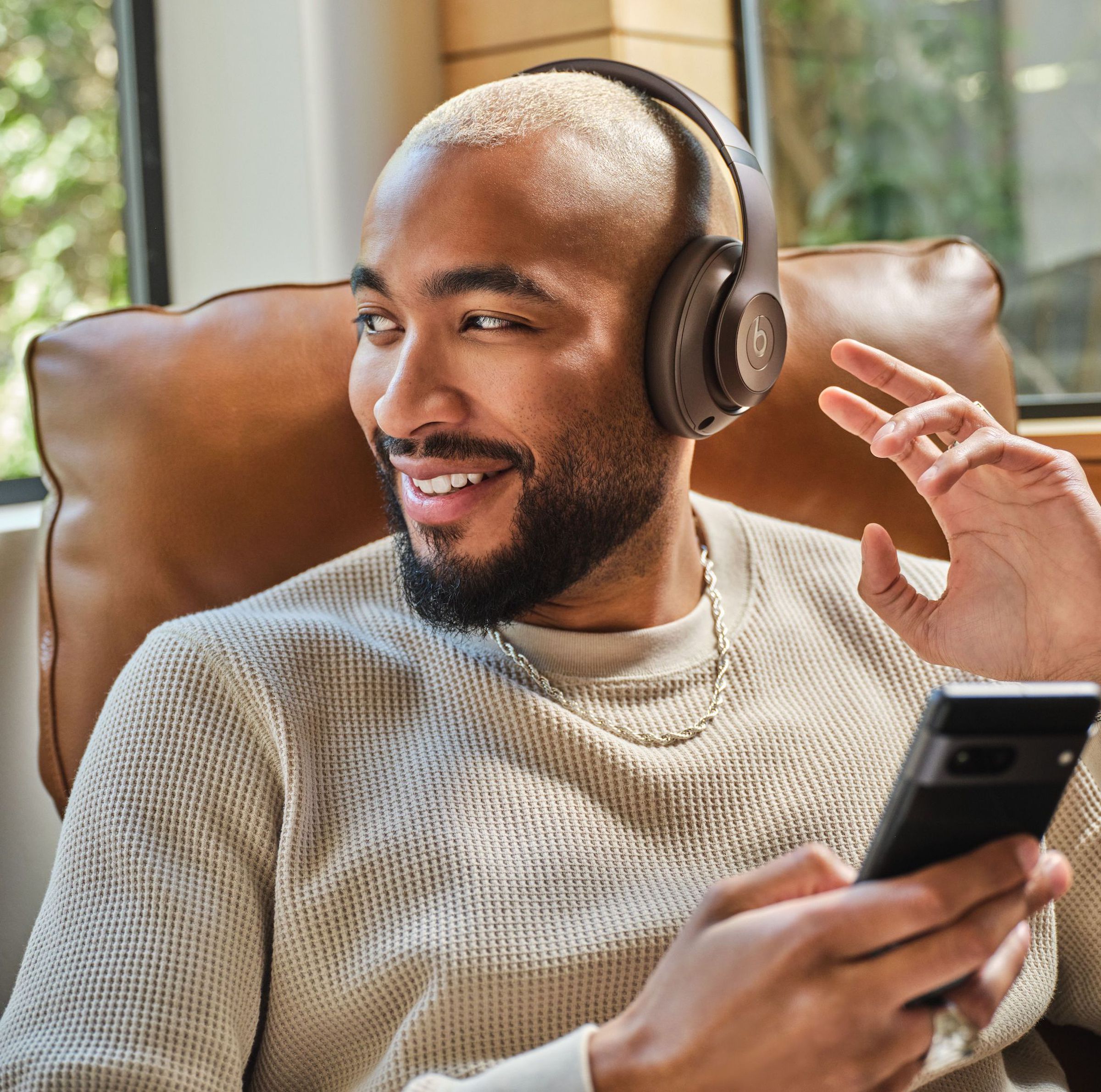 A marketing photo of a person wearing the Beats Studio Pro headphones while holding a Google Pixel 7 smartphone.