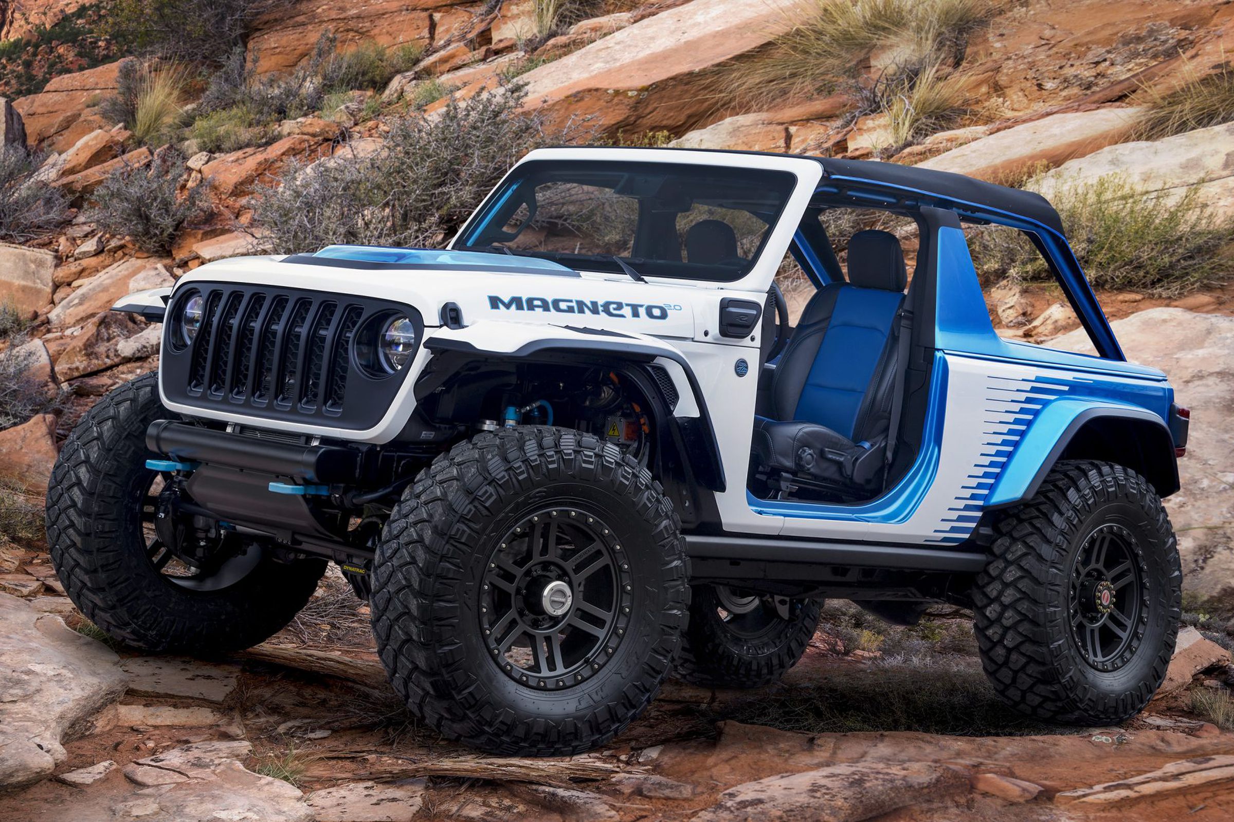 Photo of a blue and white Jeep Wrangler driving on rocks.