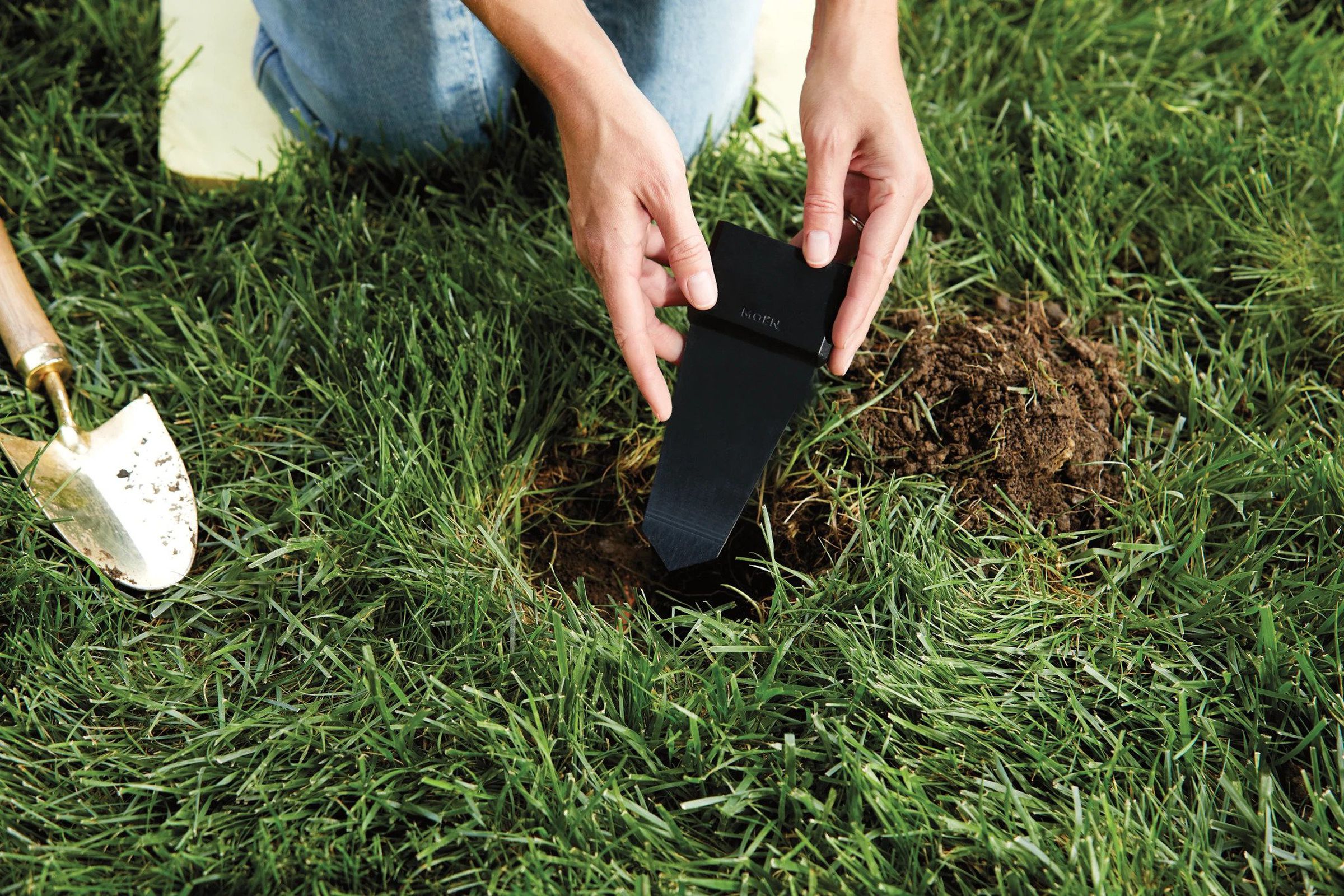 The Moen Smart Wireless Soil Sensors being placed into a hole on a lawn.