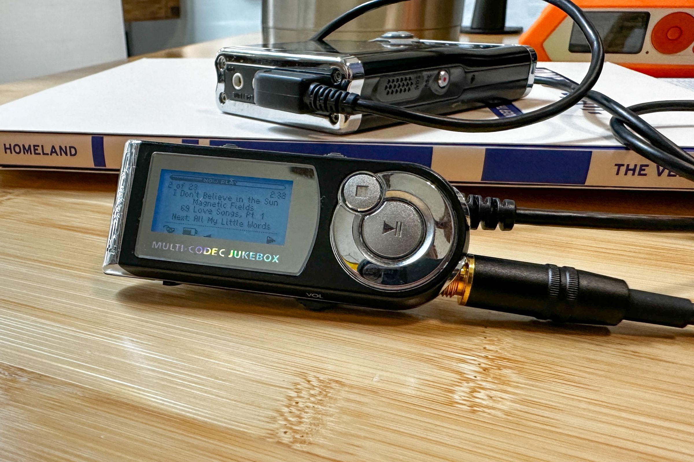 The iRiver iHP-120 wired remote on a bamboo desktop, with the main unit in the background on top of a copy of the Verge’s Homeland anthology.