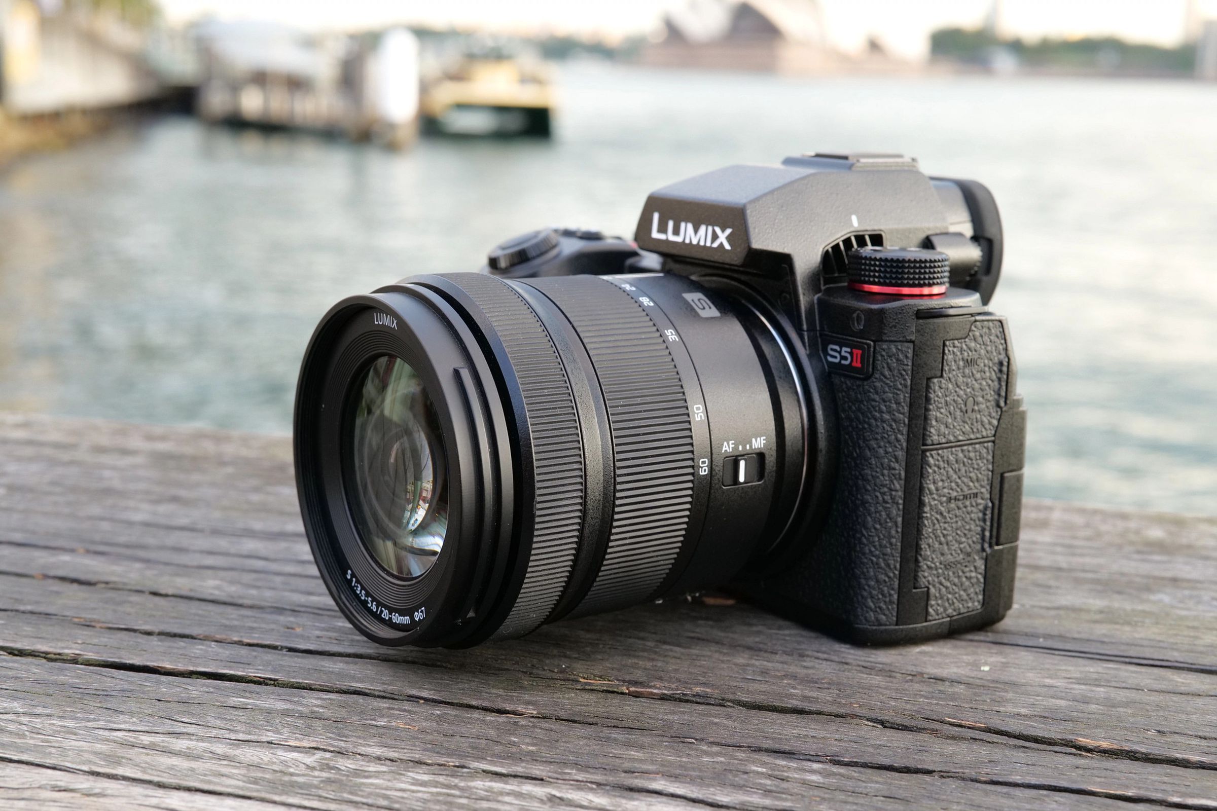 A three-quarter view of the Panasonic Lumix S5II camera, with lens attached, sitting on a wood dock in front of a body of water.