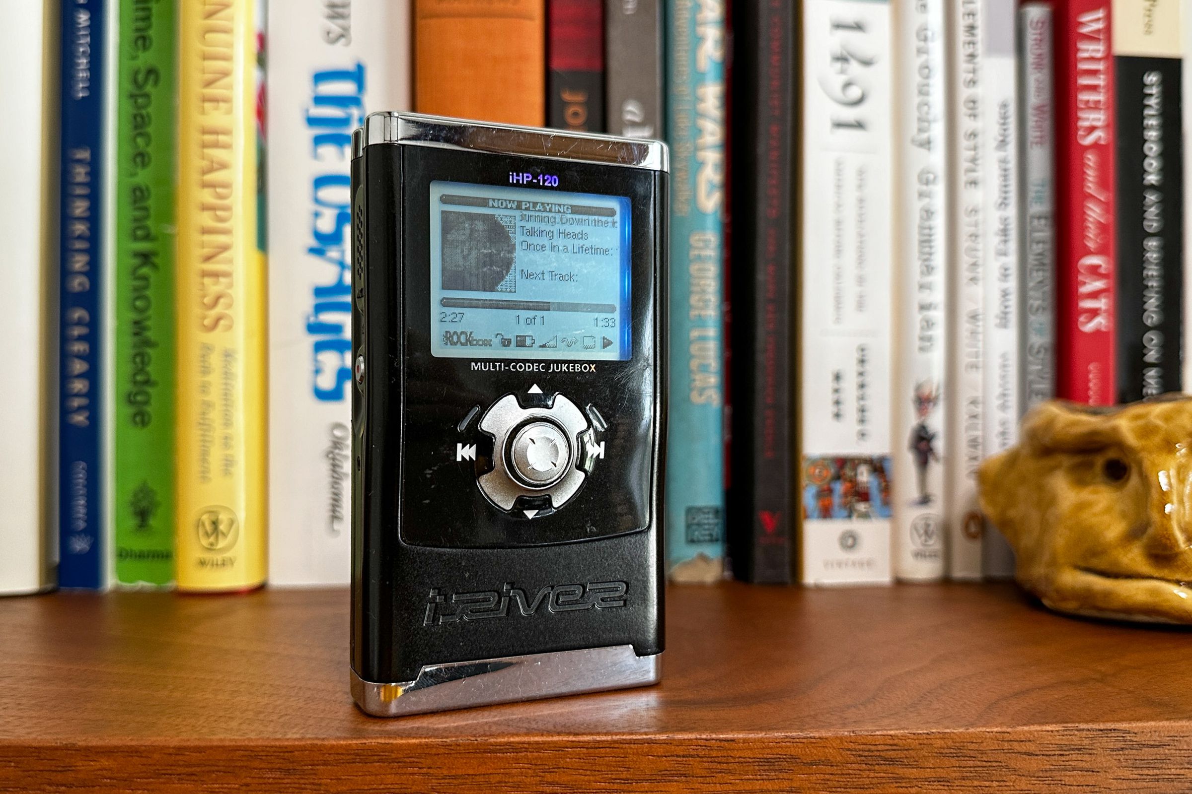 Photo of a black-and-silver MP3 player standing on a wooden shelf in front of a row of books