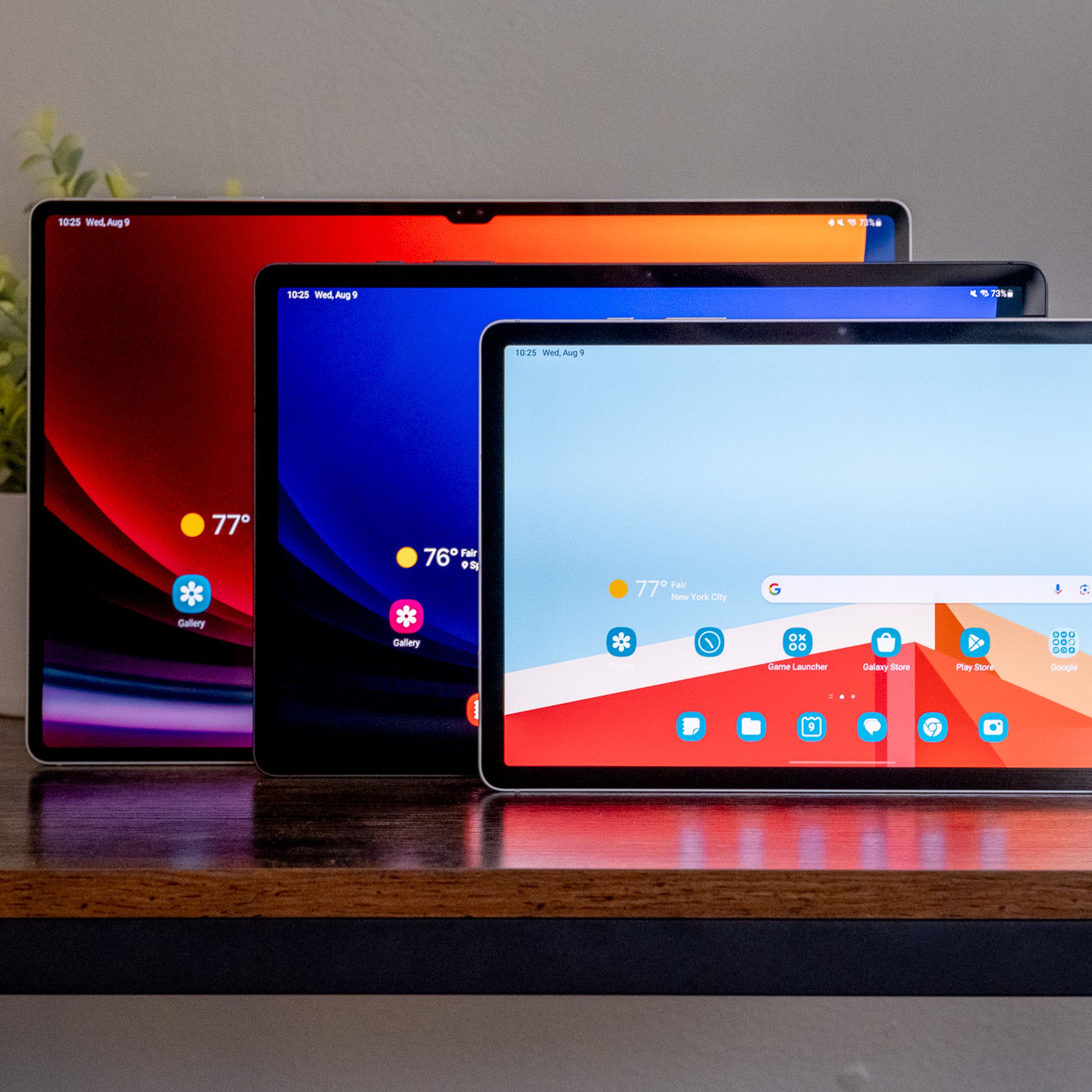 The Samsung Galaxy Tab S9, Tab S9 Plus, and Tab S9 Ultra standing in a line on a wooden desk.