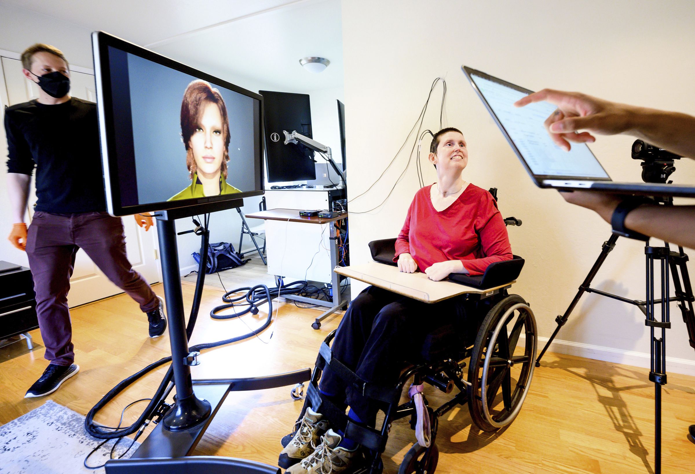 Woman suffering from paralysis from brainstem stroke next to a monitor showing a digital avatar translating her brain signals into speech.