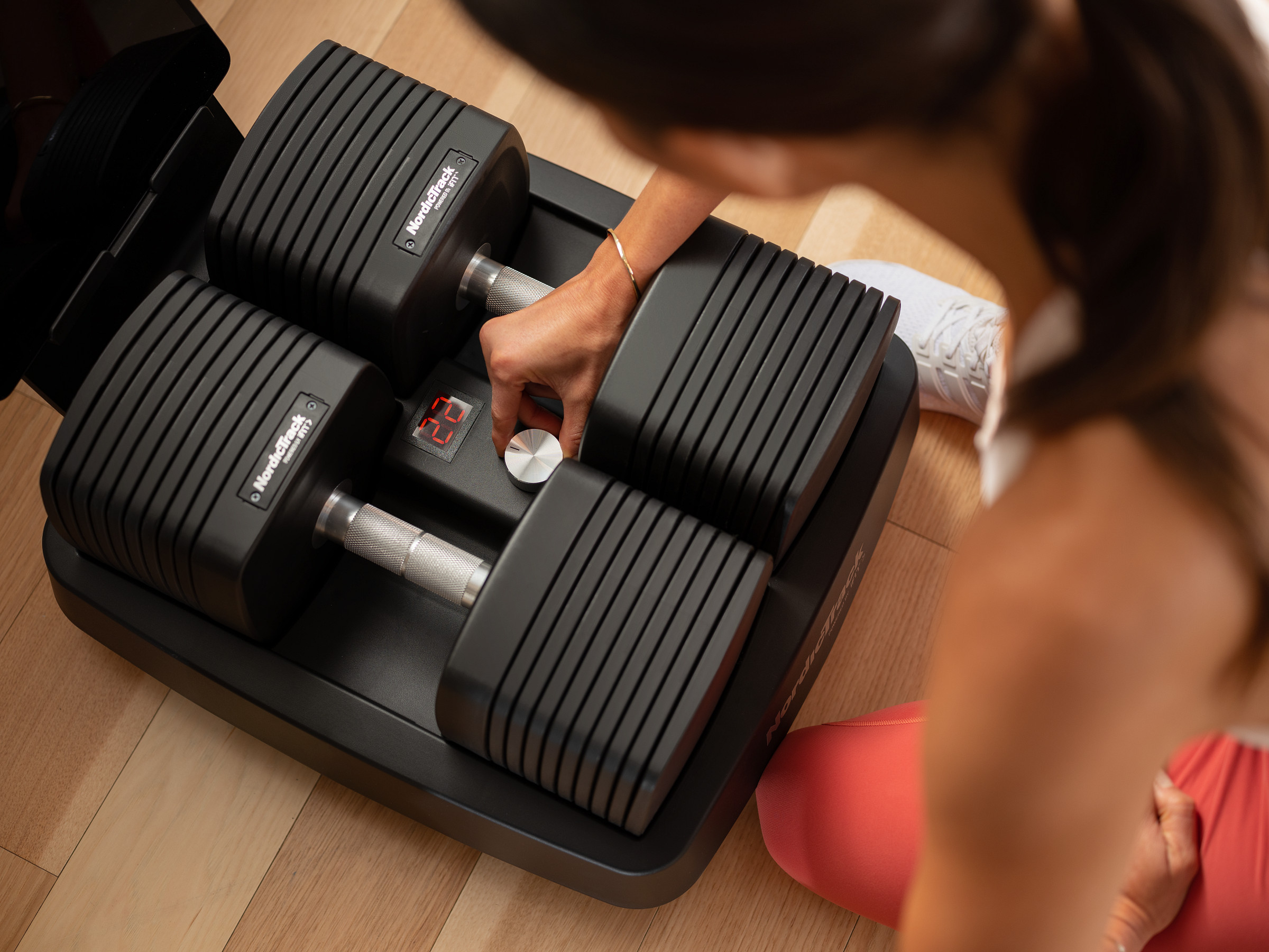 Woman turns knob embedded into the rack to adjust dumbbell weight