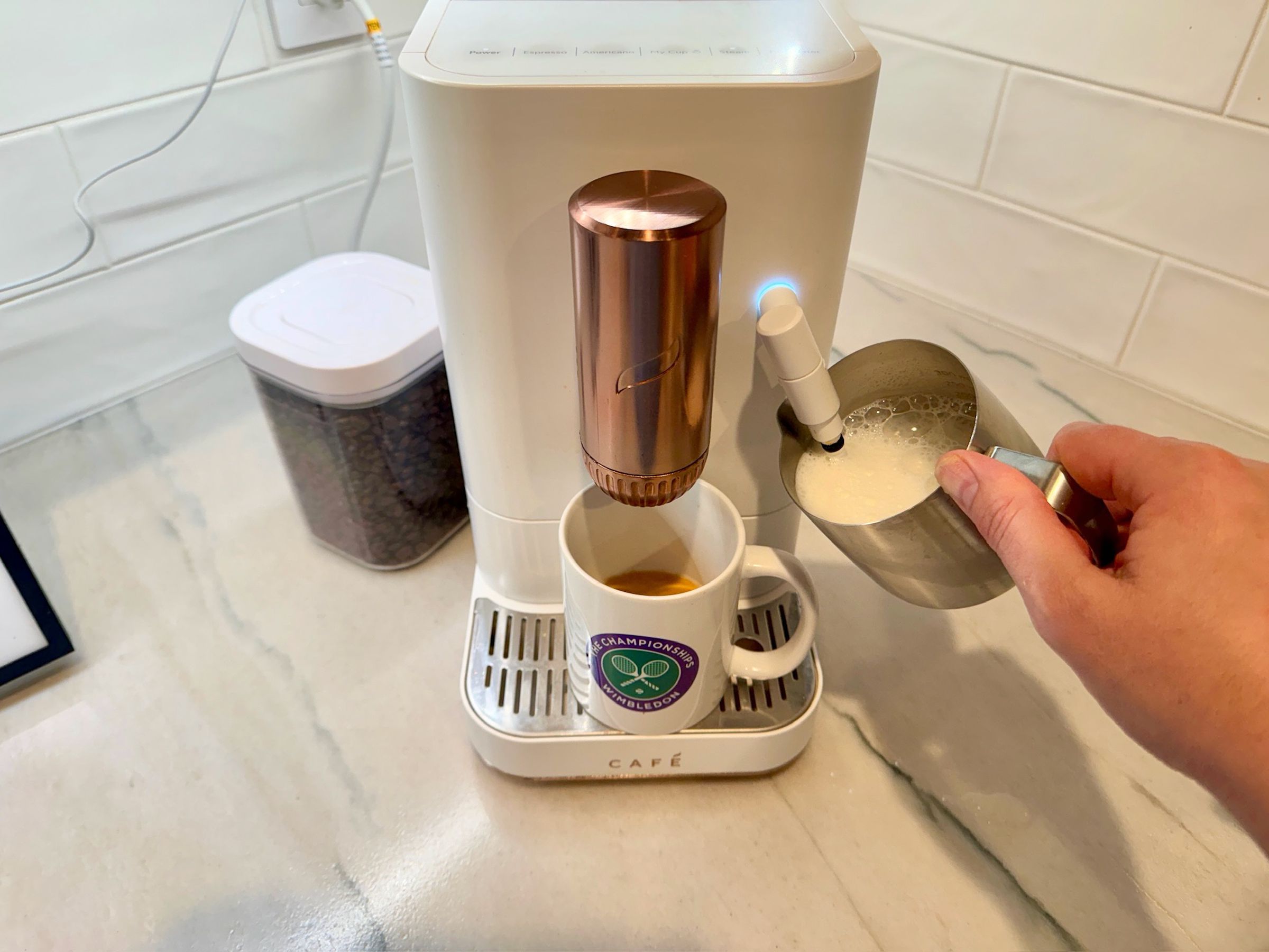 A hand frothing milk on a countertop automatic espresso maker.