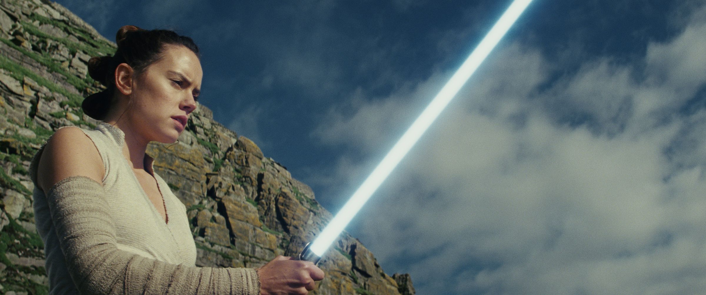 Daisy Ridley holding up a lightsaber in Star Wars: The Last Jedi.
