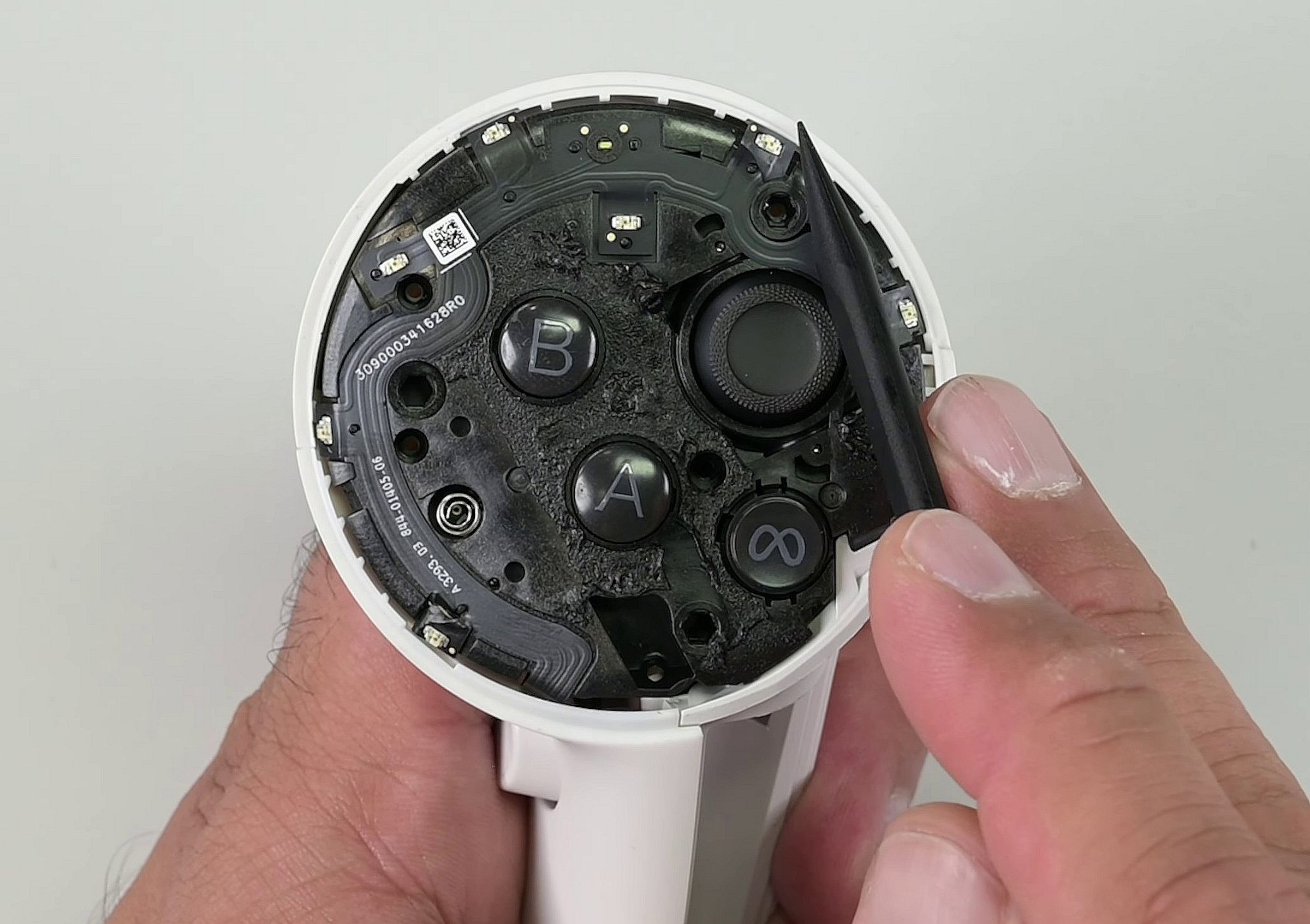 The top of the controller open, revealing a black expanse atop, which is melted glue, a ribbon cable, and seven infrared LEDs