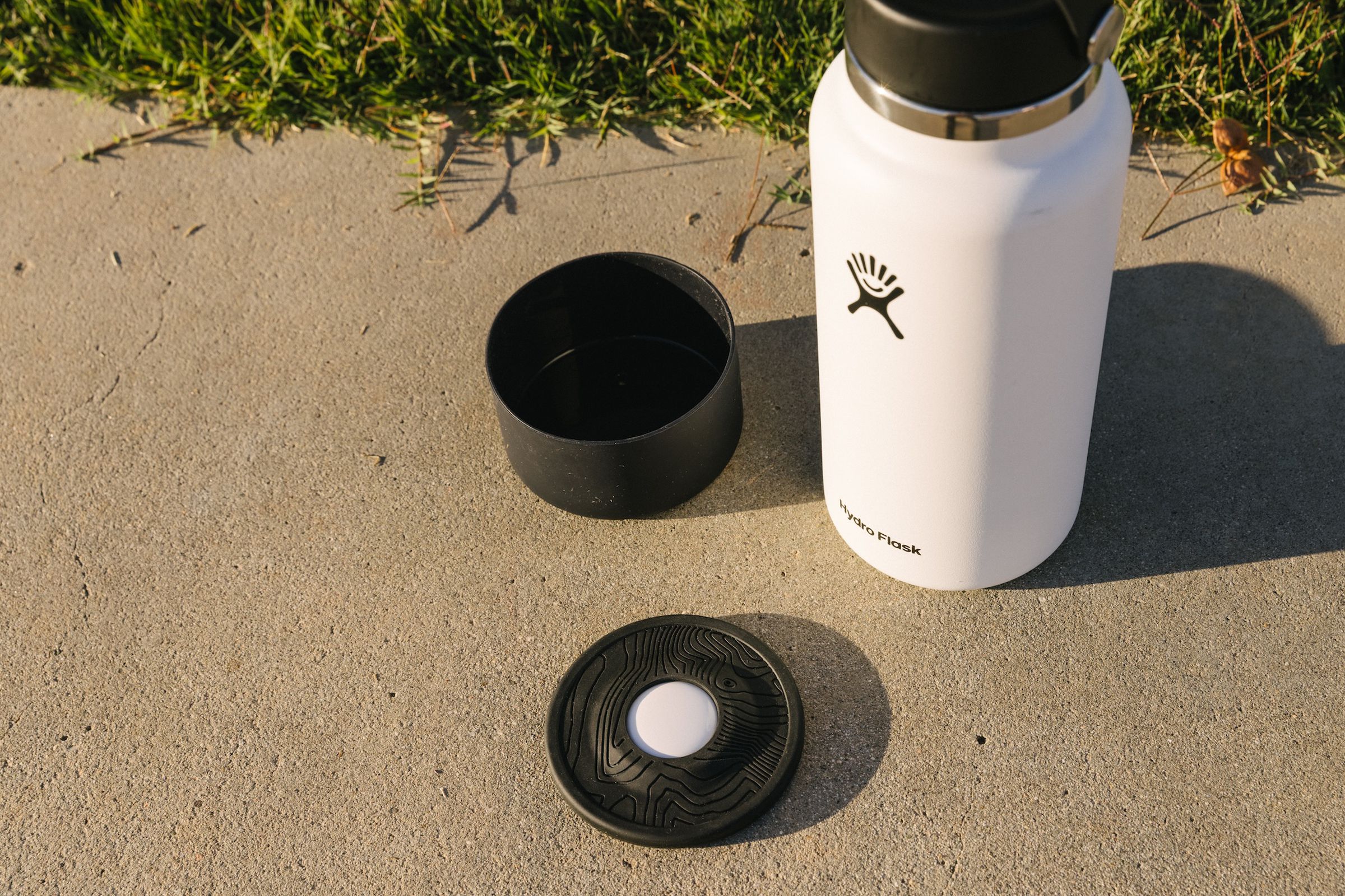 A picture of the Hydro Flask on a concrete surface, next to a Flex Boot and a Hydro Flask Tracker, which has an AirTag sitting in it.