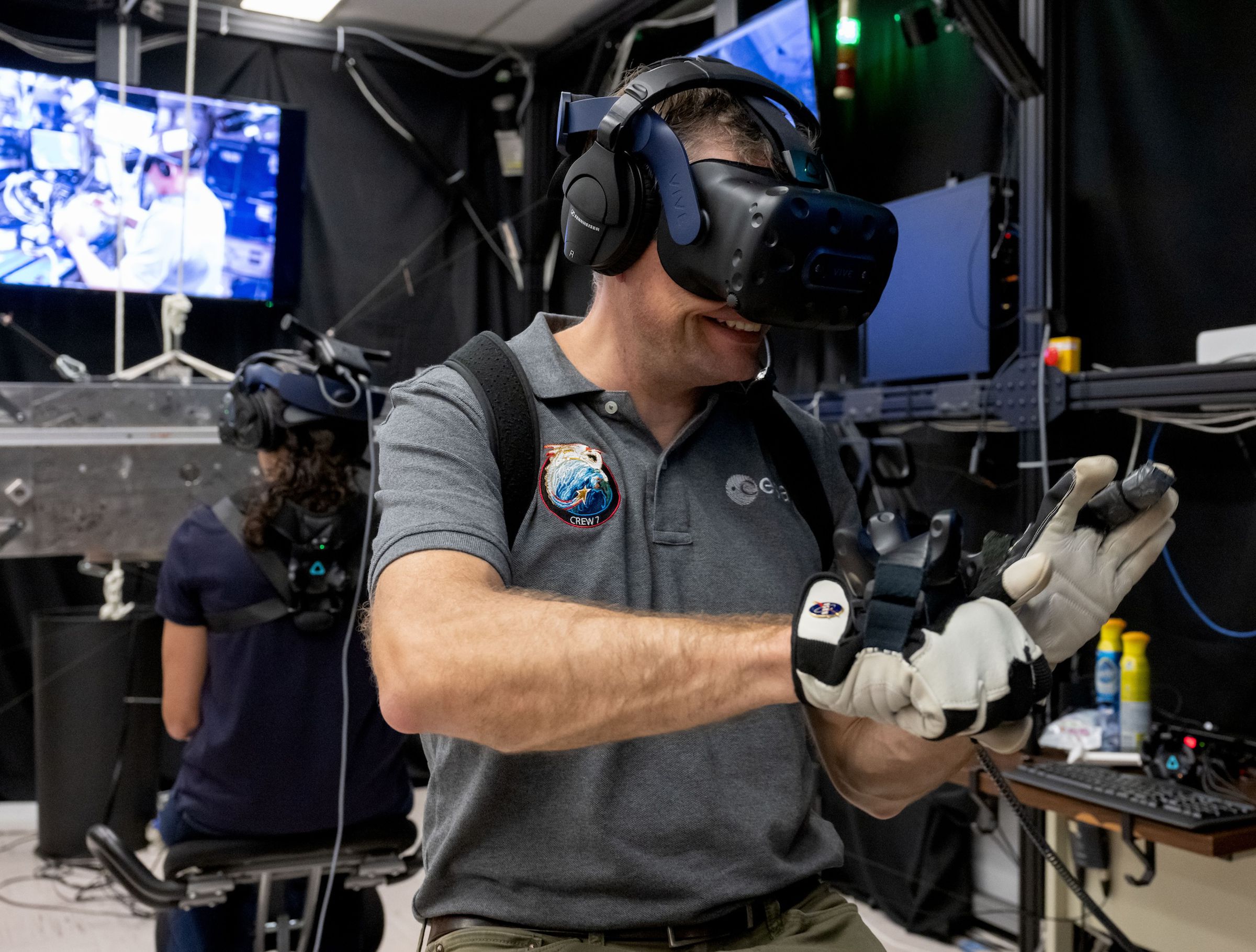 A person wearing a virtual reality headset and gloves, mimicking movements needed to repair equipment during a spacewalk.