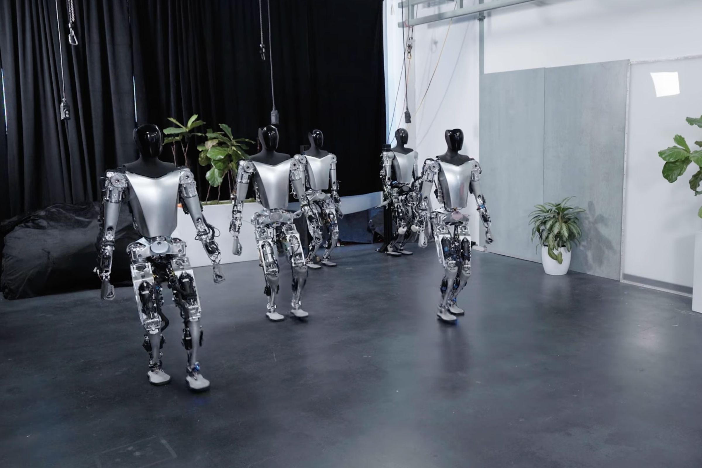 Five Tesla bots walking in a fancy warehouse building towards the camera