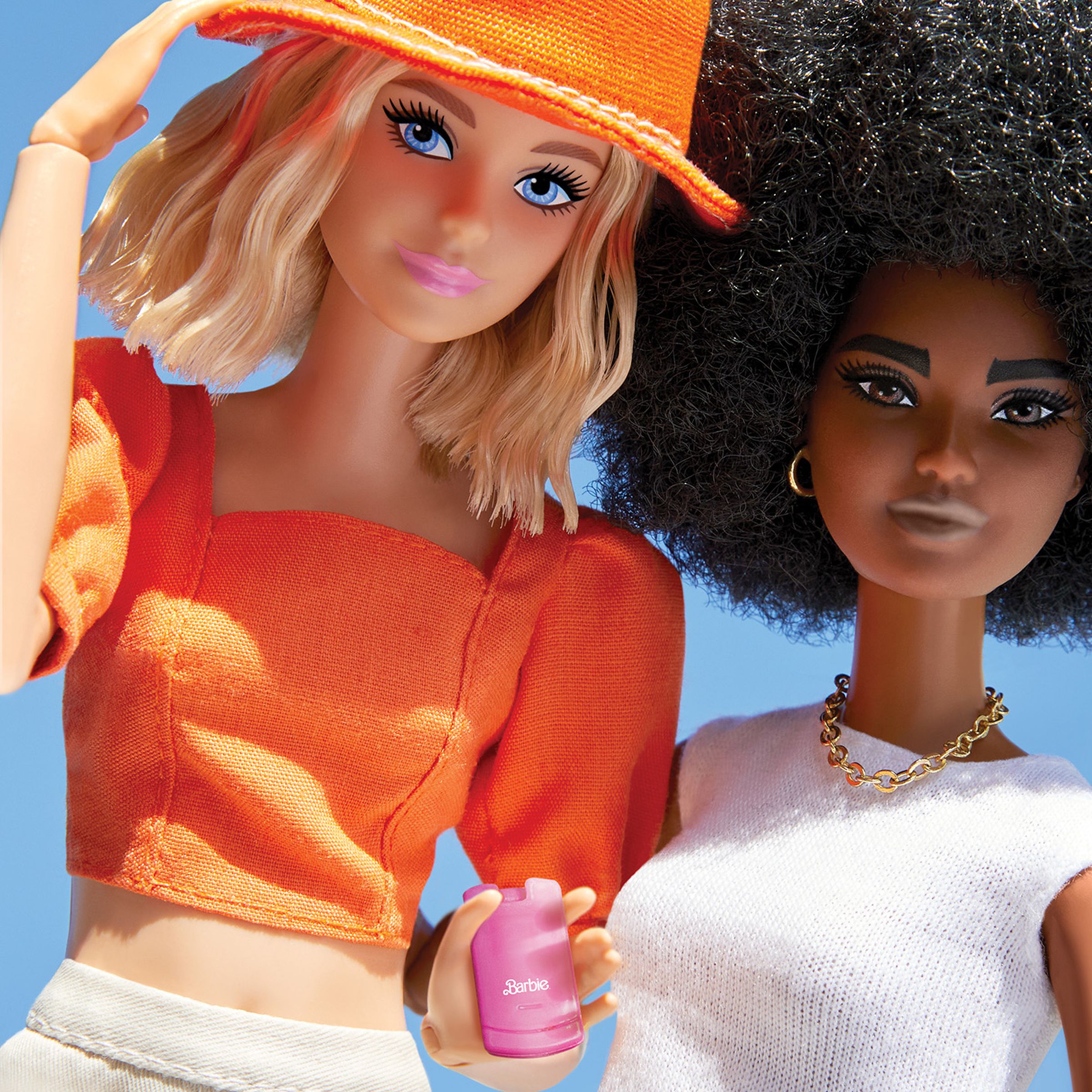 Two barbie dolls, one holding a toy phone.