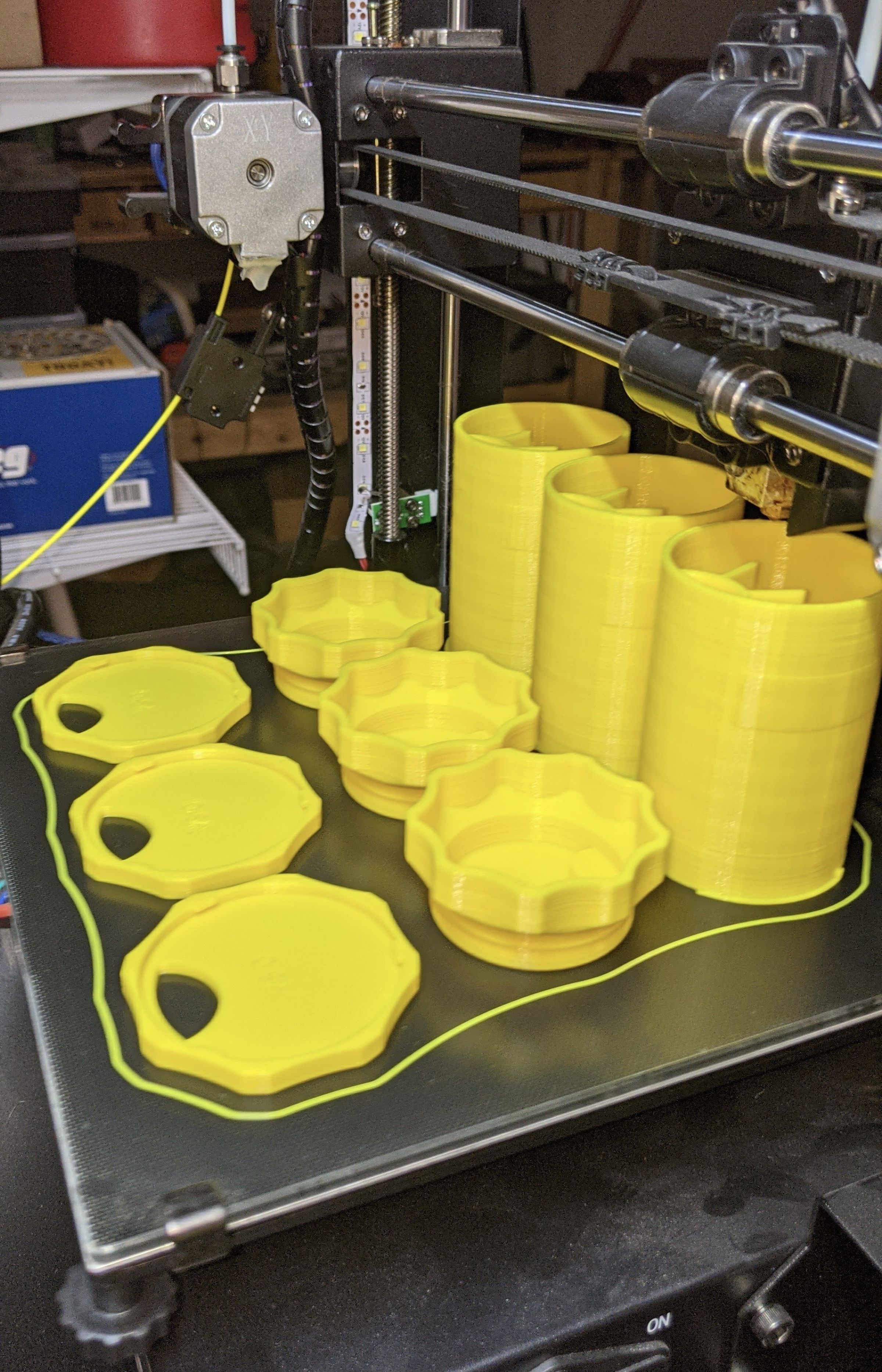 Three yellow bottle bodies, three caps, and three bases sitting on a 3D printer.