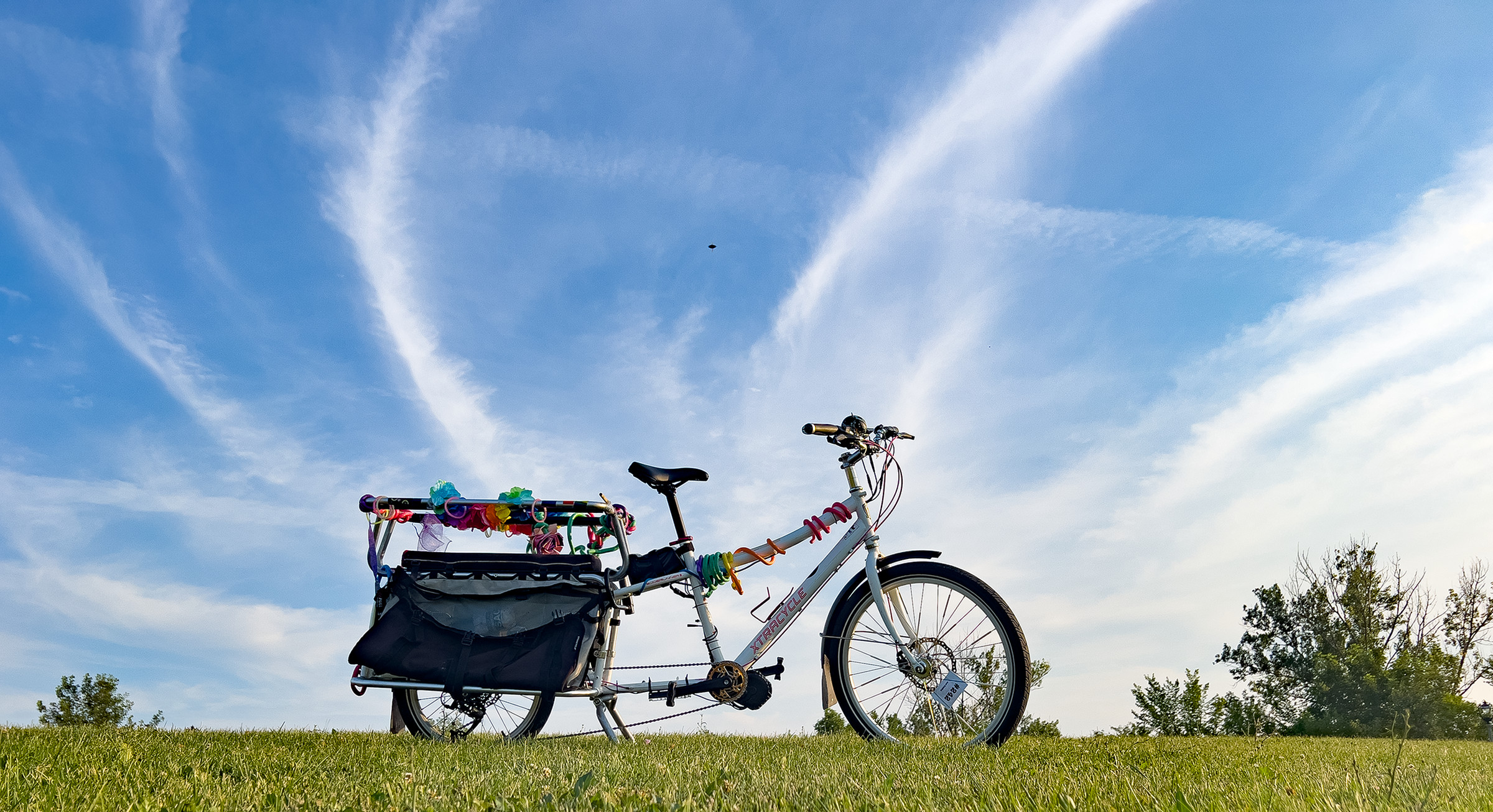 A picture of the bike sitting on a grassy hill. Behind it, a blue sky is filled with wispy, thin clouds stretching over the bike.