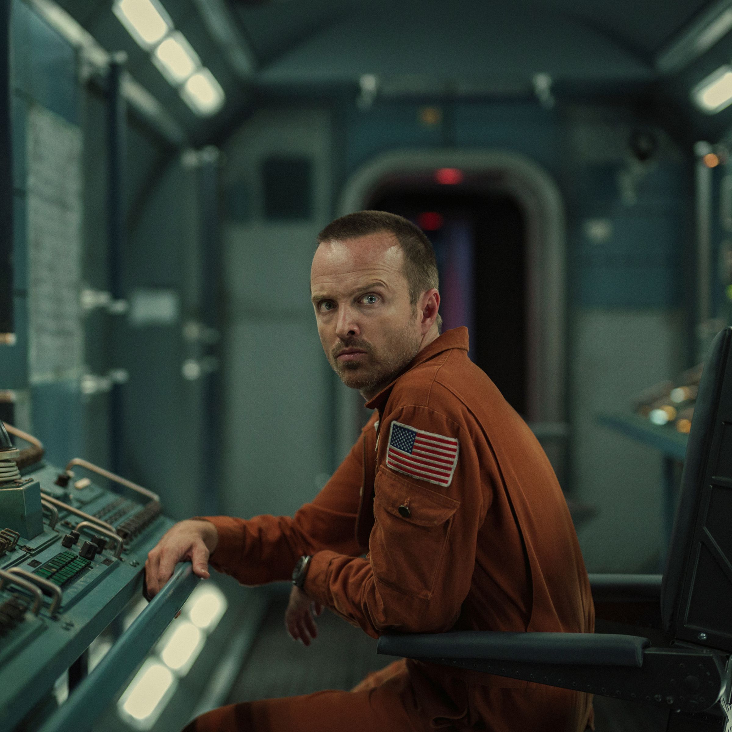 An image of actor Aaron Paul at a board of 1960s spaceship controls.