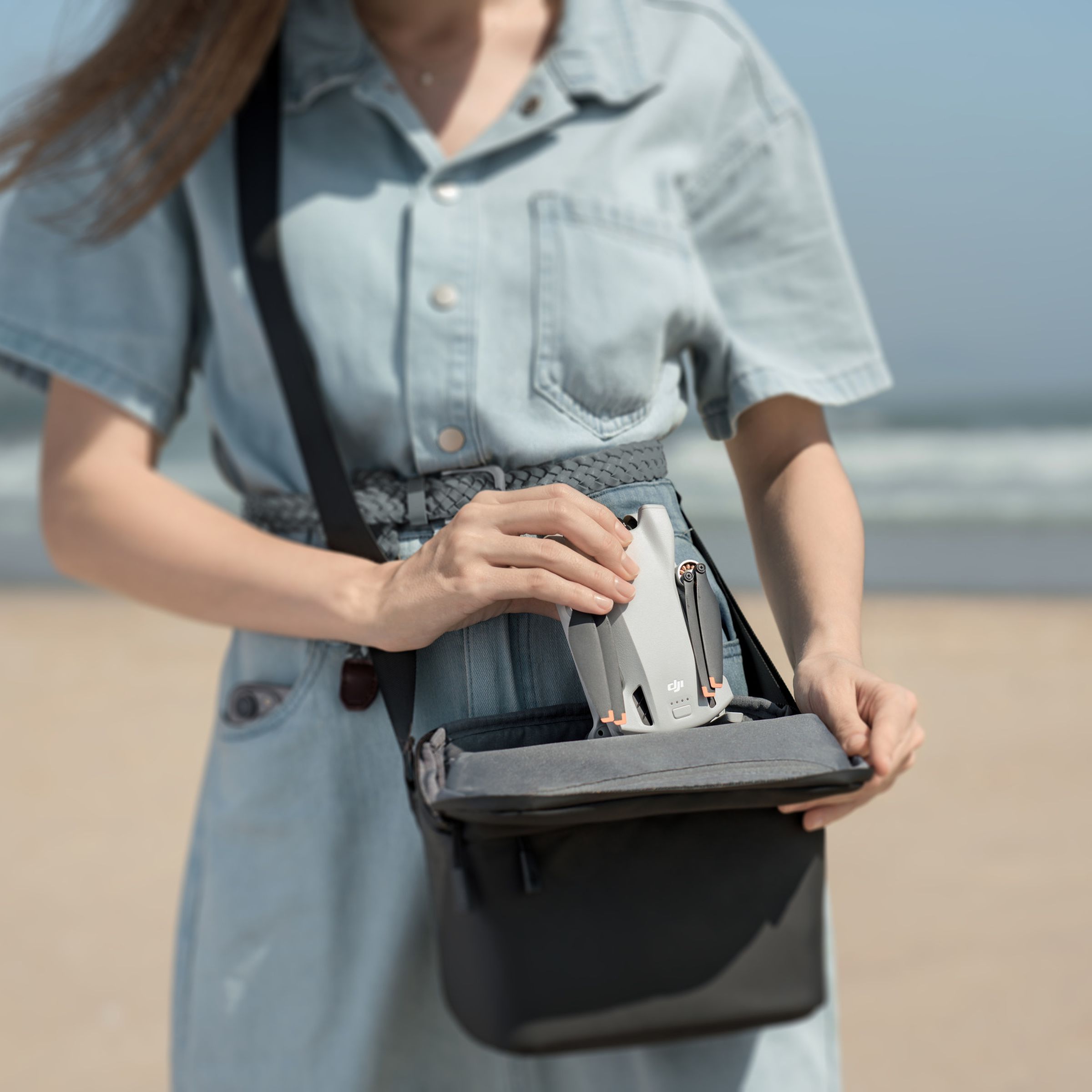 A person on the beach, placing a compacted DJI Mini 3 drone into an average sized handbag.
