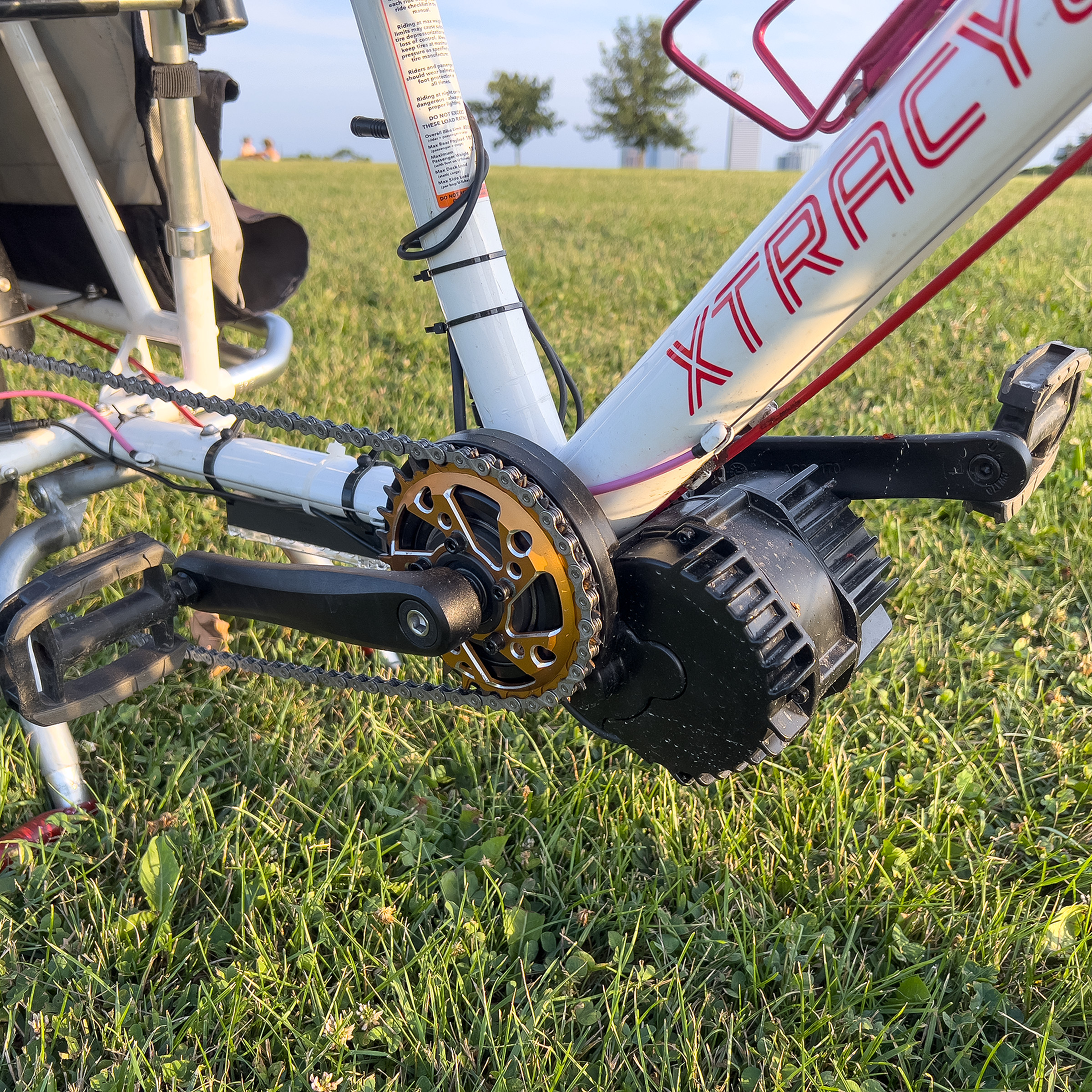 A close-up of the bike’s bottom bracket section after it was finished. It has the e-bike motor, new chainring, and new chain installed. It is sitting in a grassy field at sunset.