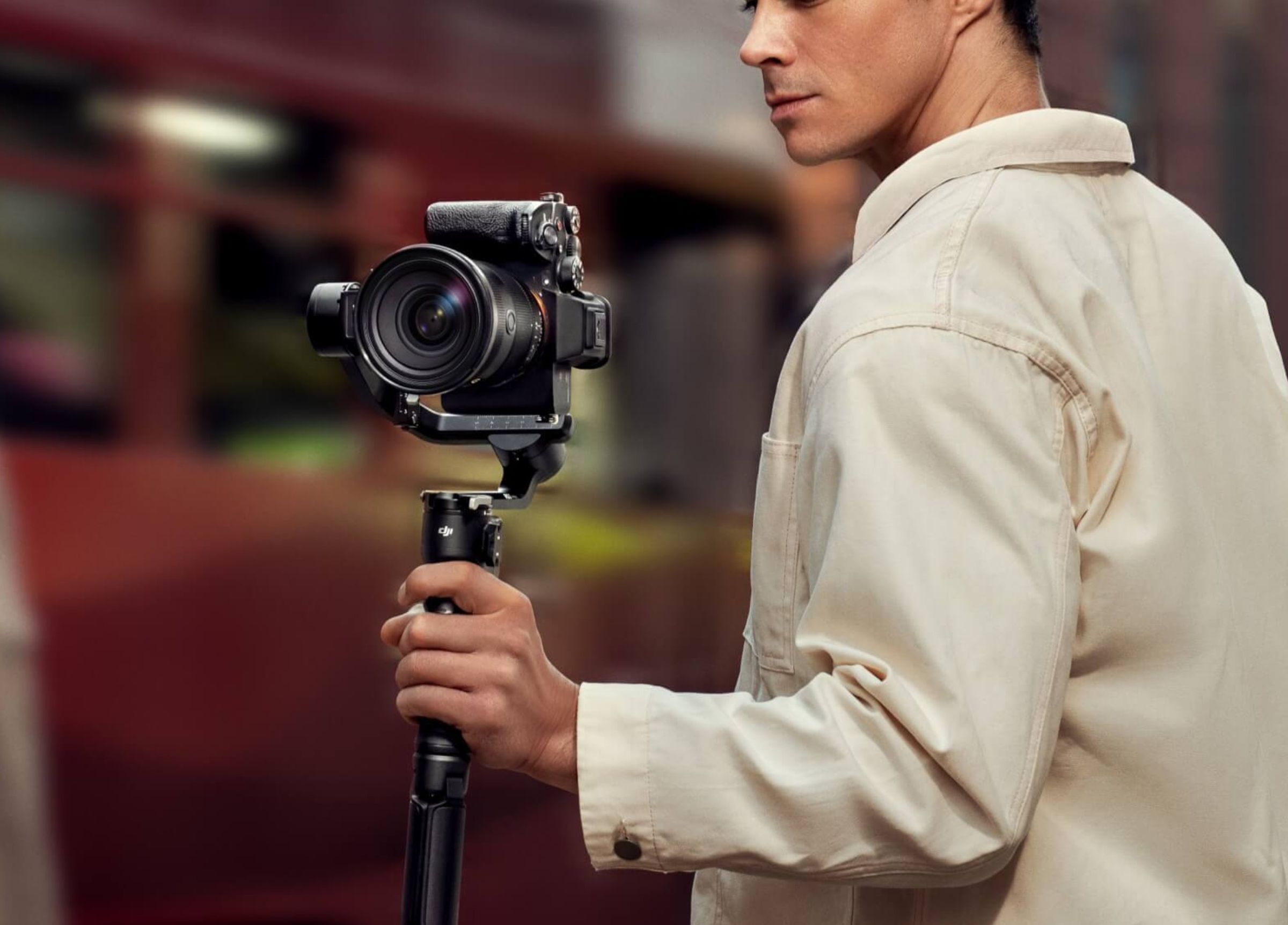 A man holding the DJI RS 3 Mini with a DSLR camera equipped in one hand while shooting footage outside.