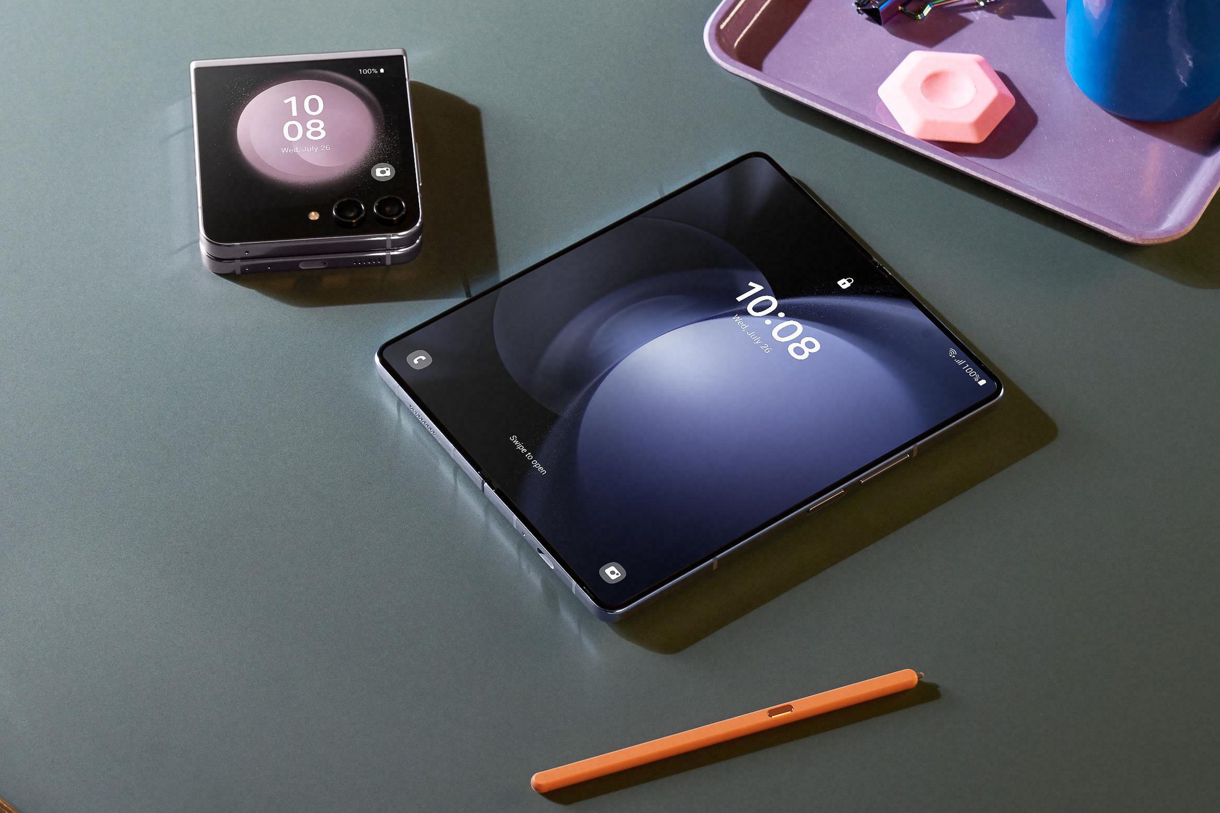A closed Samsung Galaxy Z Flip 5 and an open Galaxy Z Fold 5 sitting on a table near a tray and a stylus.